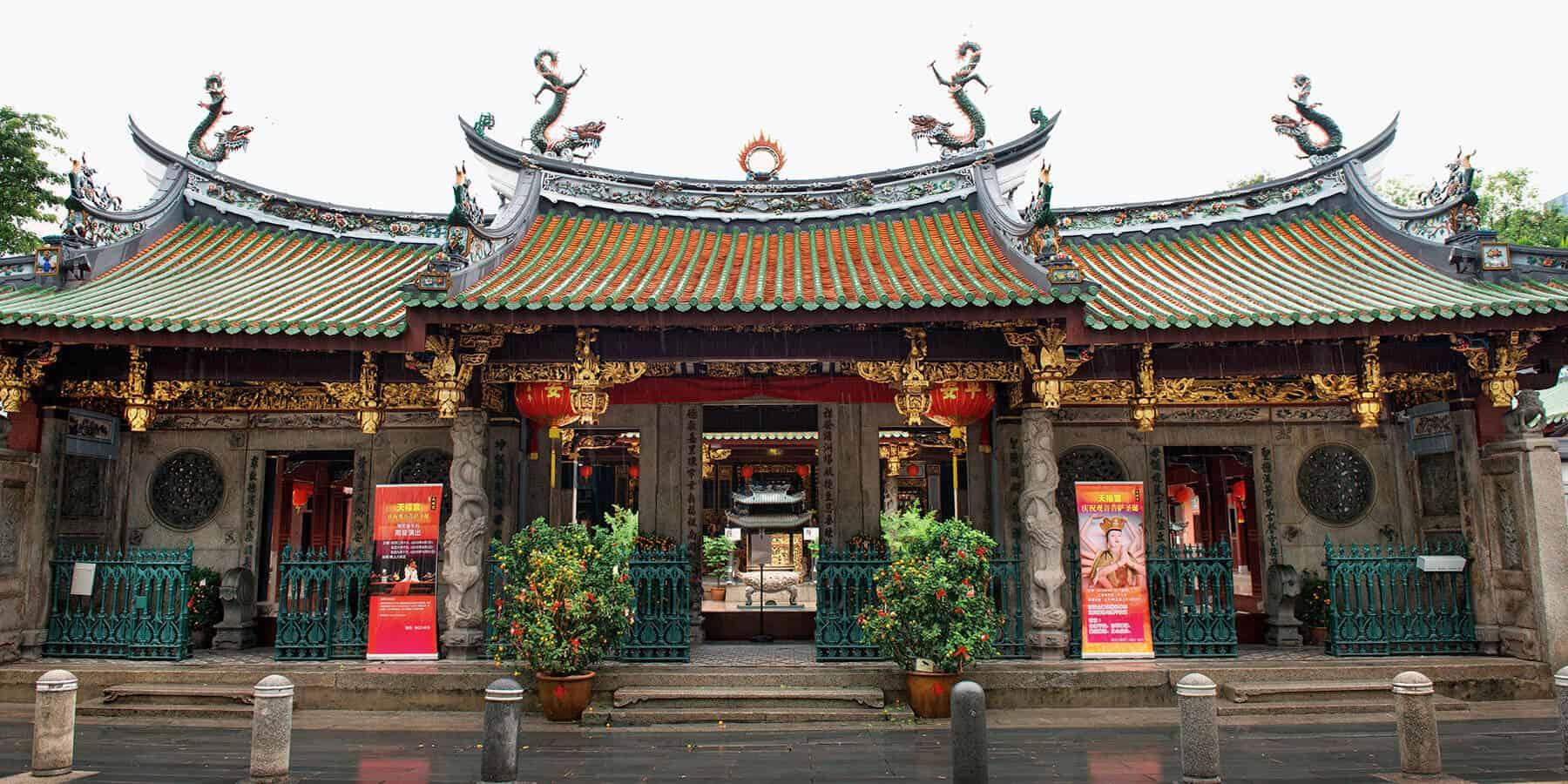 Exterior facade of Thian Hock Keng Temple in Singapore, featuring ornate sweeping roofs, dragon finials, red lanterns, and traditional Chinese architectural details