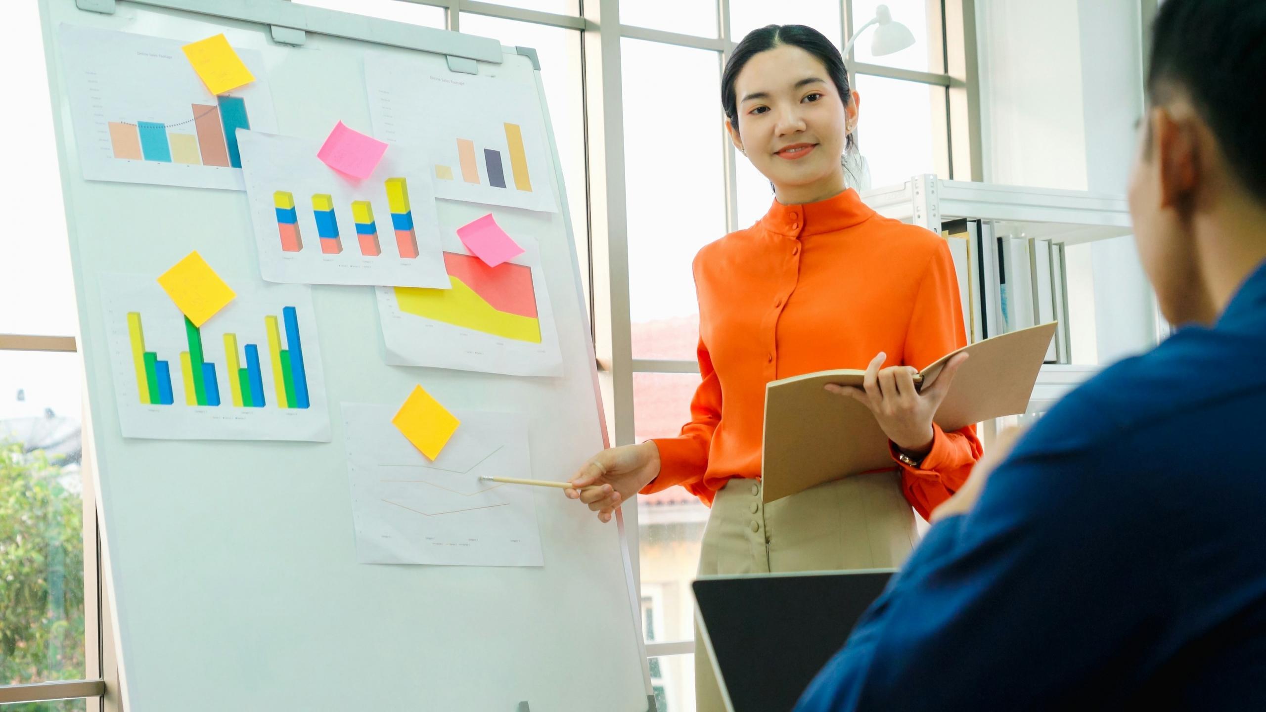 woman standing over a board with graphs training a group of people