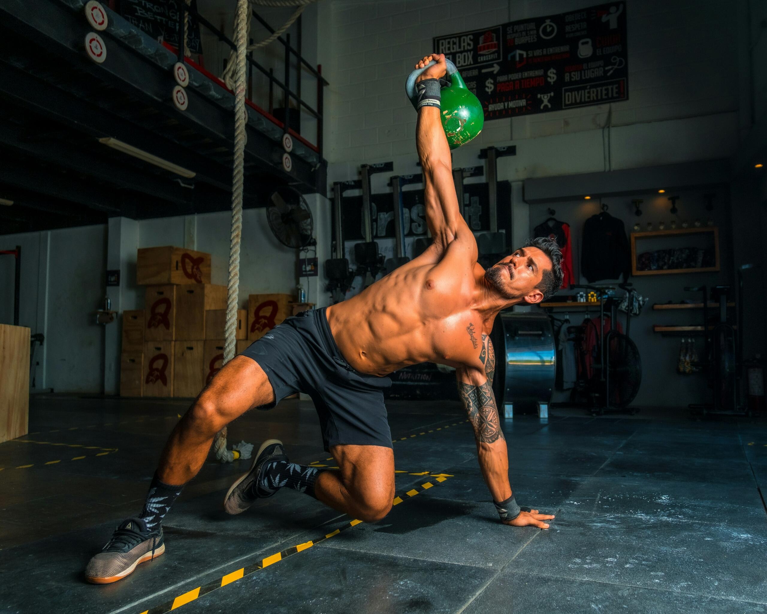 a slika prikazuje moškega med izvajanjem kettlebell vaje v fitnes centru.