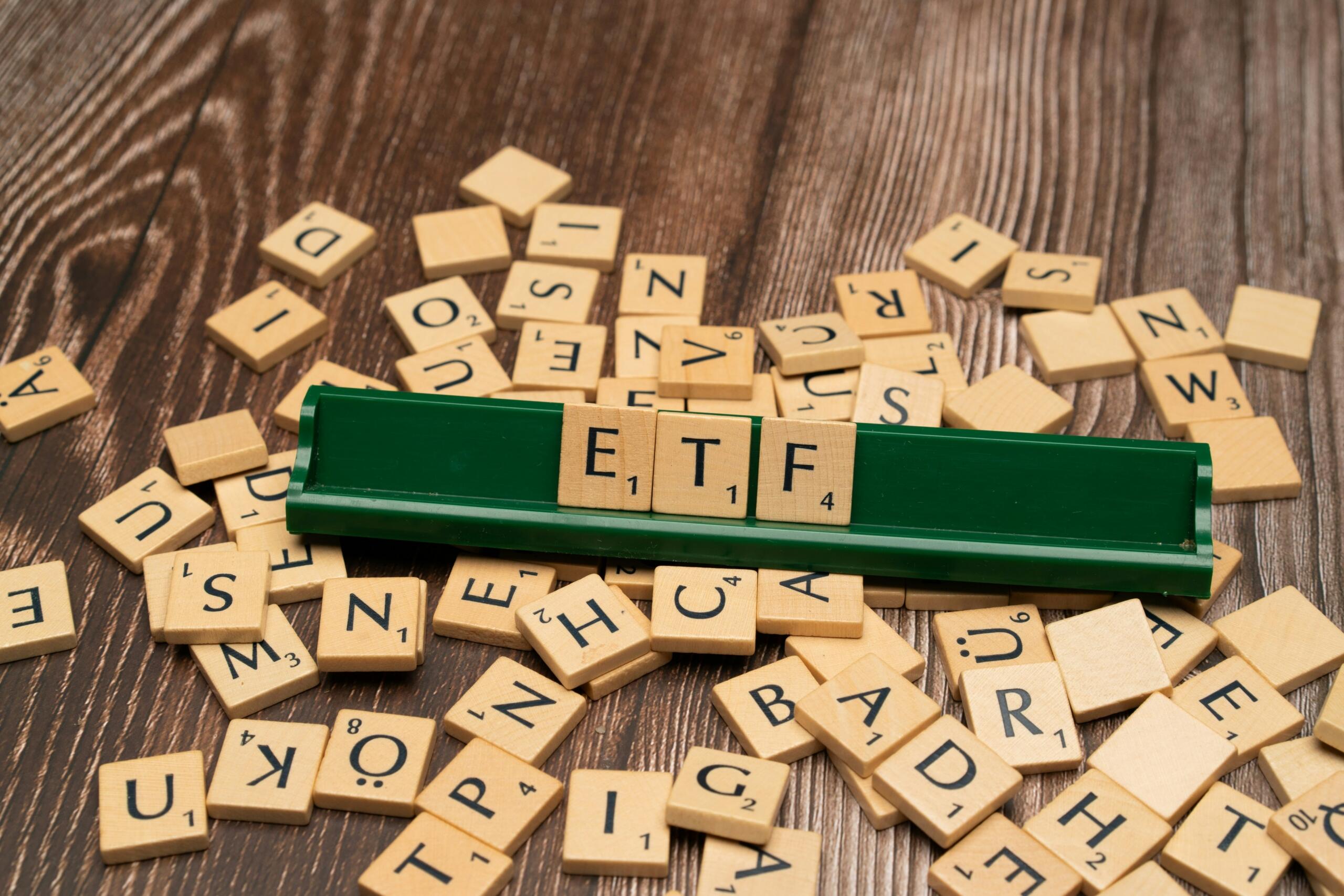 Scrabble ploščice, ki tvorijo besedo 'ETF' z razmetanimi črkami na leseni površini.