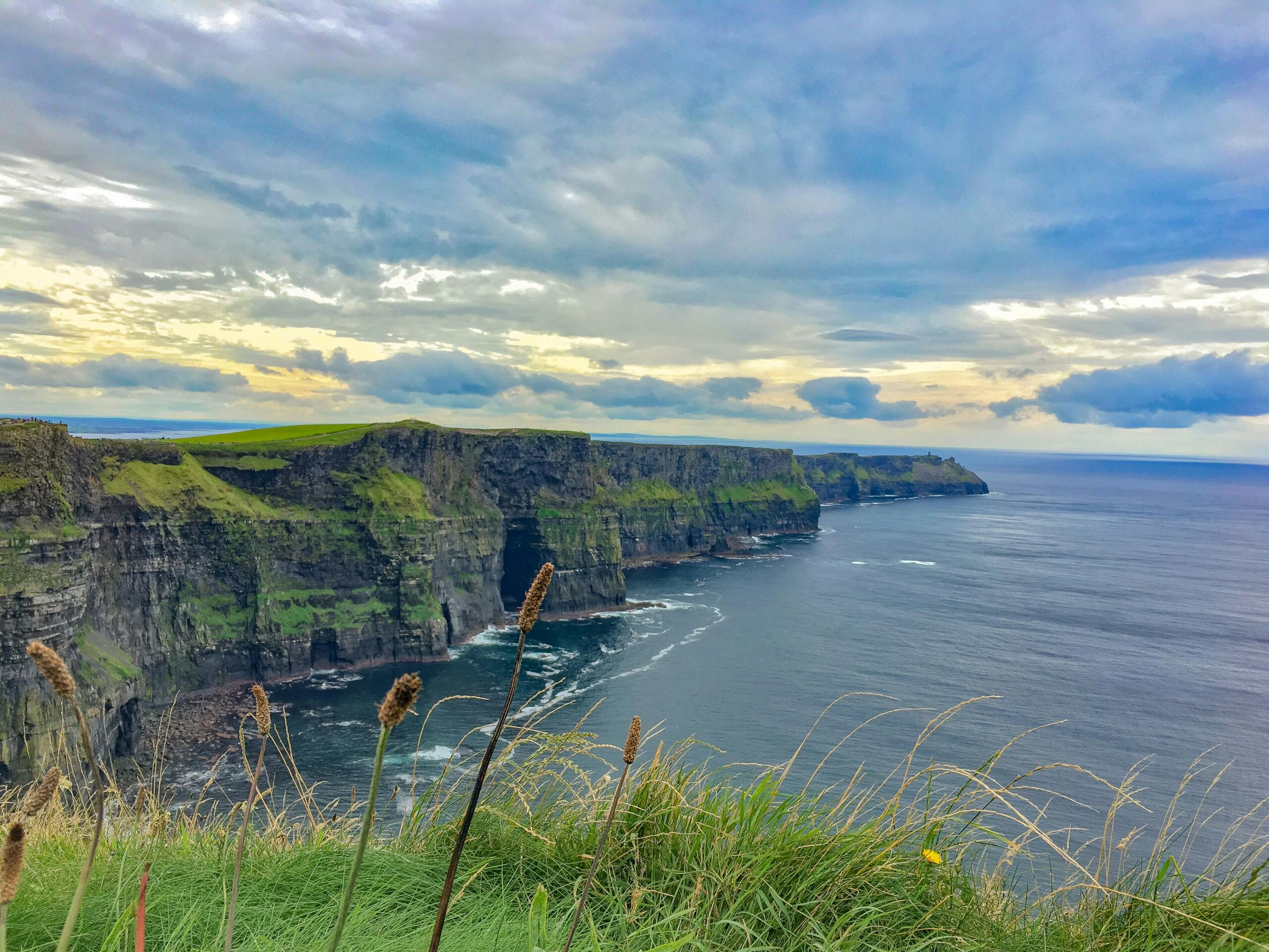 Dramatični Cliffs of Moher z visokimi pečinami, zelenimi griči in mavrico nad zalivi in otoki pod modrim nebom