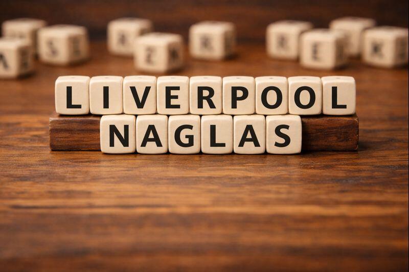 Lesene črkovne kocke na mizi, ki sestavljajo napis »LIVERPOOL NAGLAS«.