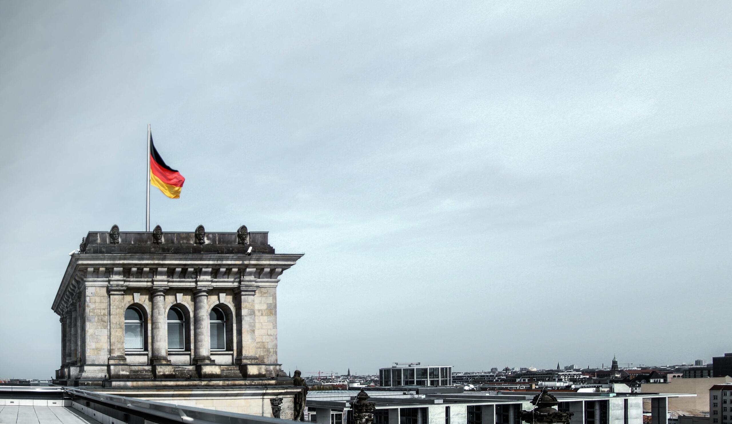 Nemški parlament Reichstag z nemško zastavo, ki plapola na vetru nad panoramo Berlina
