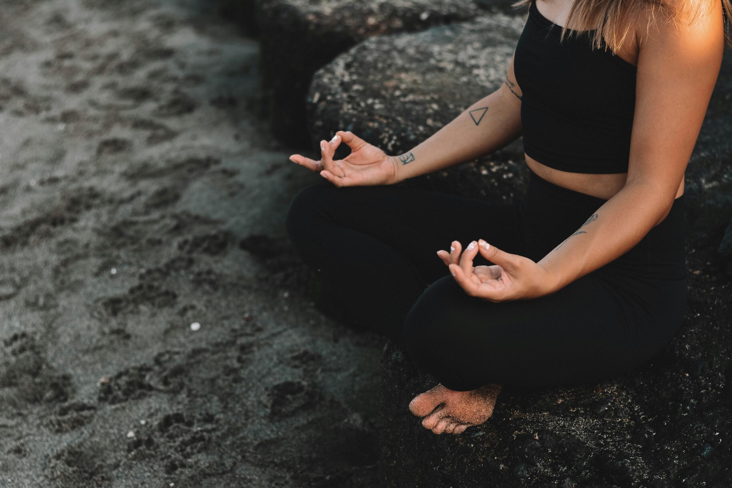 Oseba izvaja meditacijo in dihalne vaje med sedenjem ob morski obali.