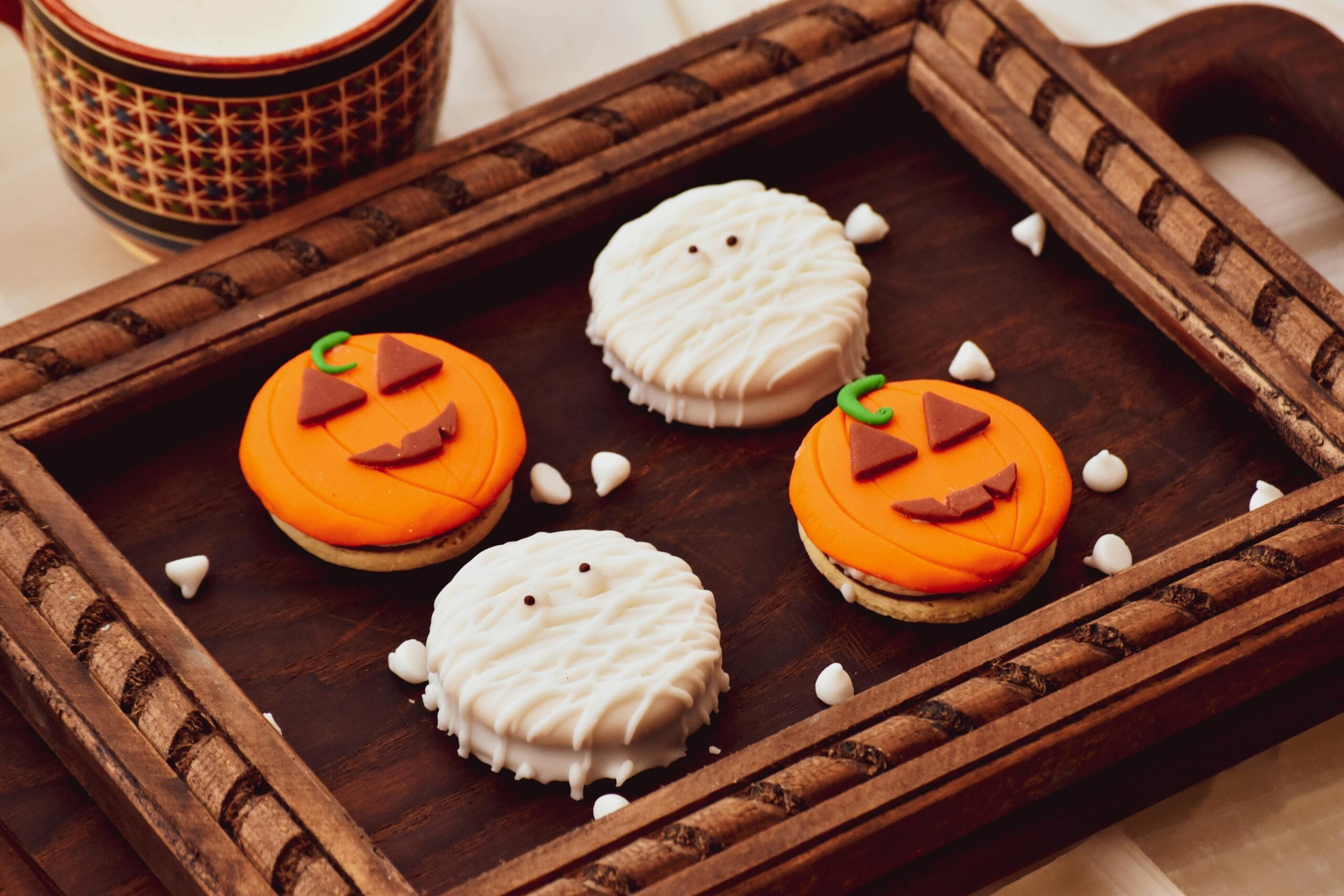 Halloween piškoti v obliki buč in mumij na lesenem pladnju.
