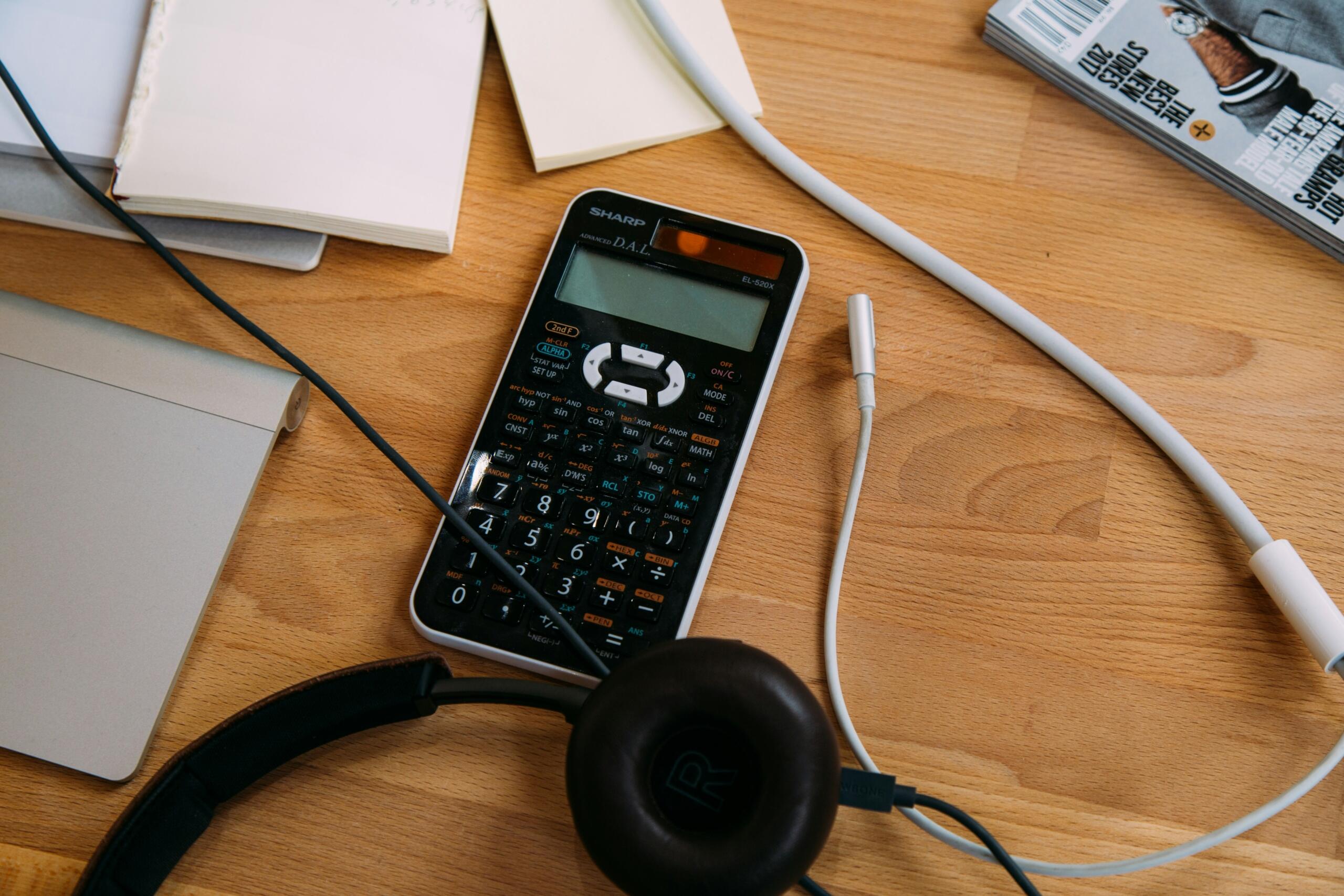 Kalkulator, slušalke in učni pripomočki na delovni mizi za spletno učenje matematike.