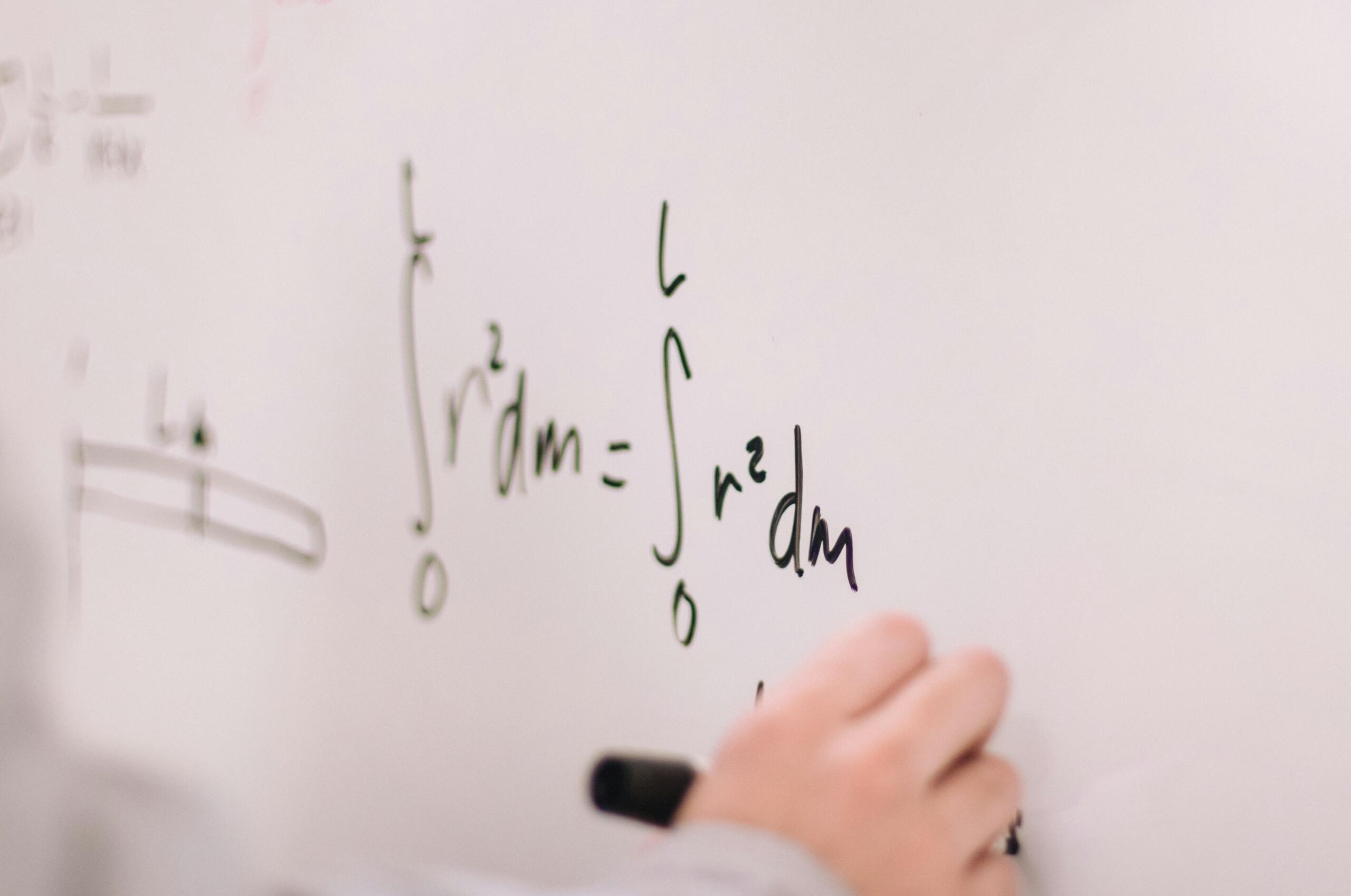 Roka zapisuje matematično enačbo na belo tablo med razlago snovi.