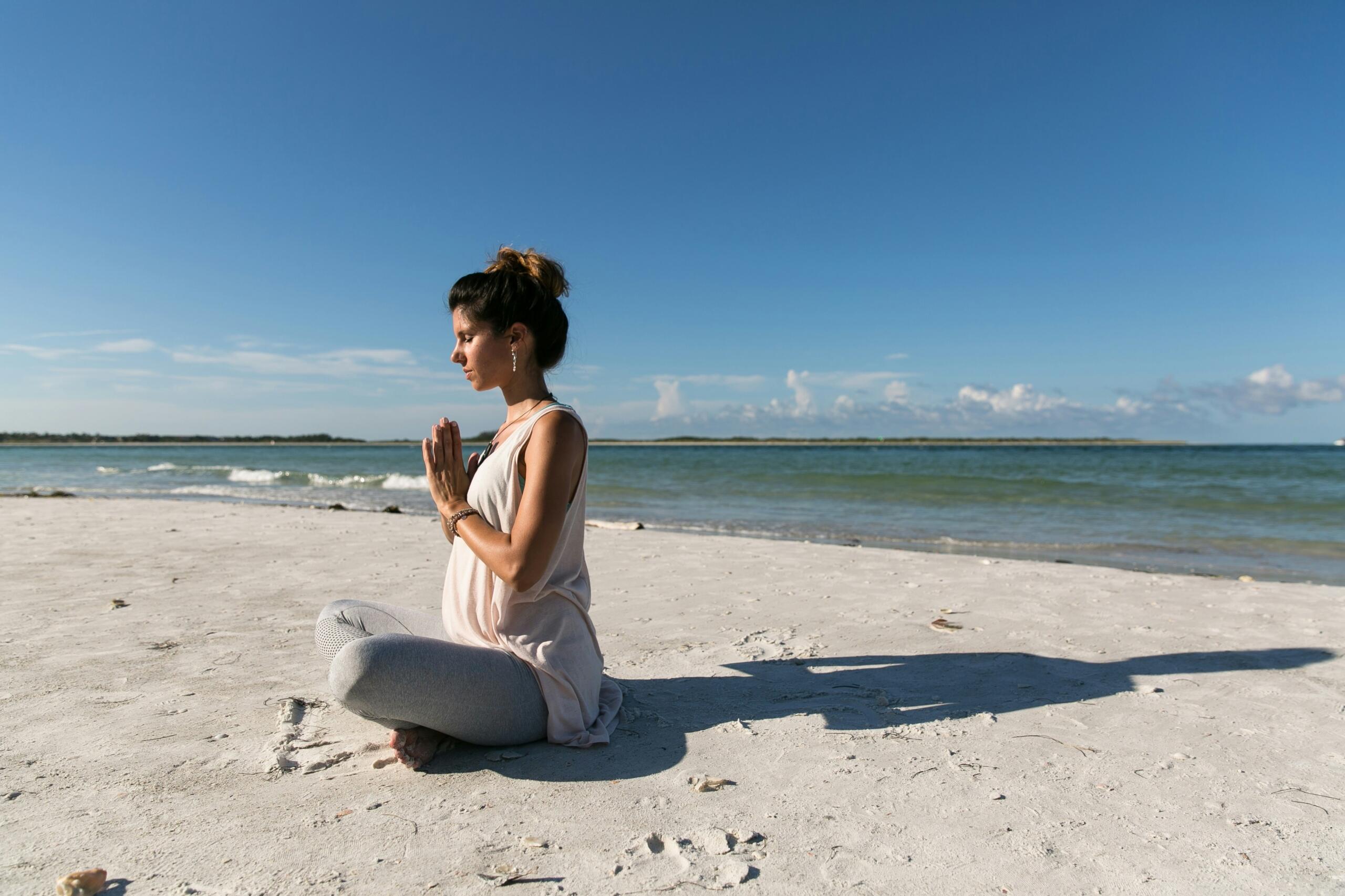 Ženska meditira na peščeni plaži ob morju in izvaja umirjeno dihanje.