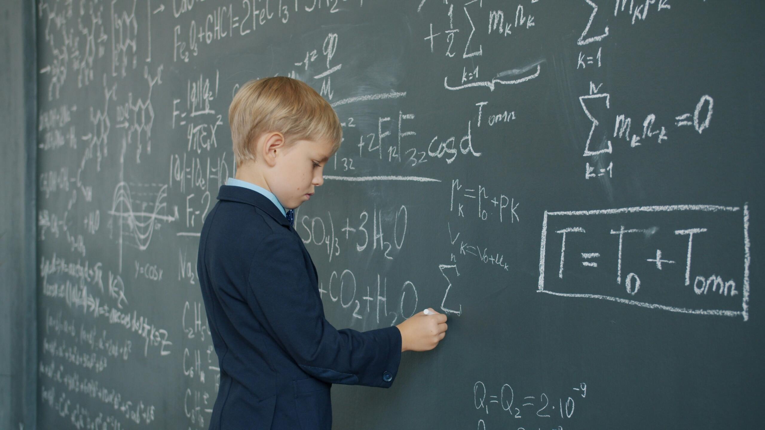 Otrok stoji pred tablo in rešuje matematične enačbe.