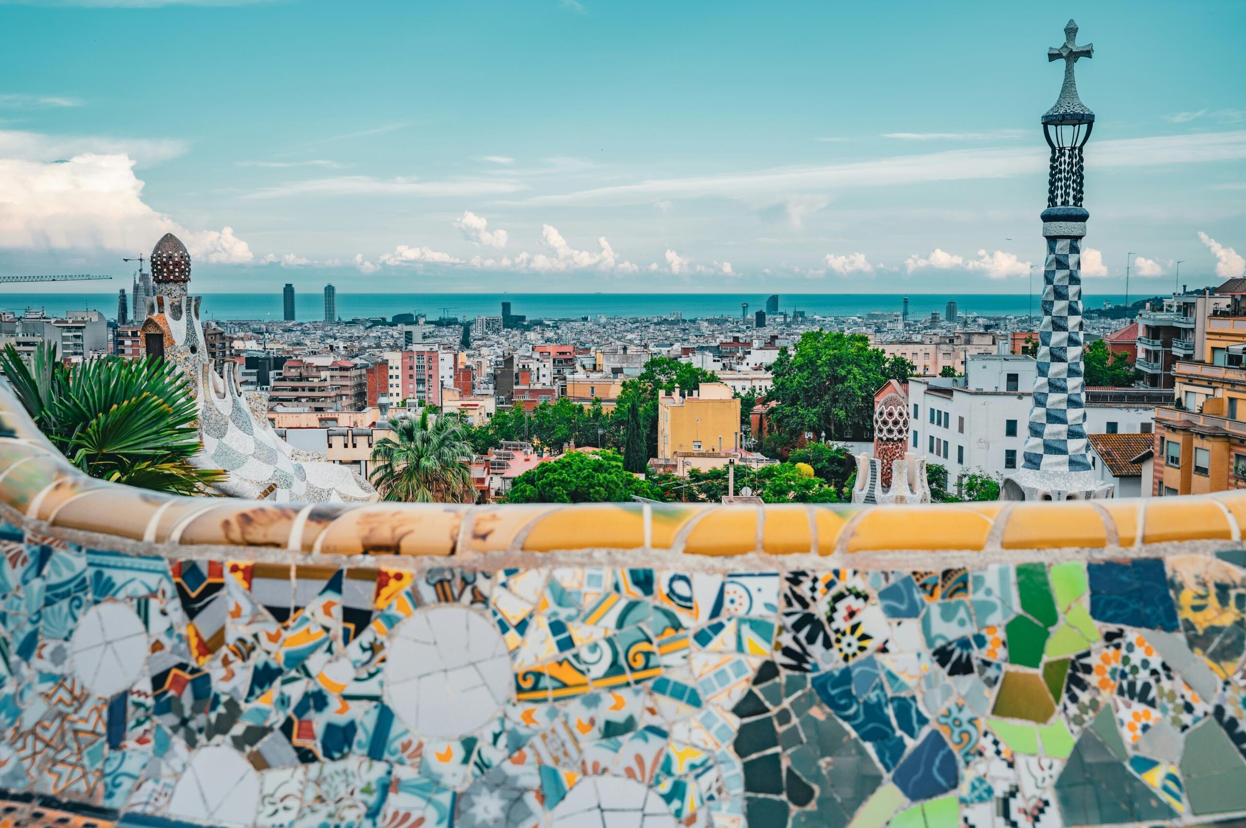 Pogled na barcelonsko panoramo z Mediteranskim morjem v ozadju iz Parka Güell z mozaičnim ograjem in Gaudíjevima stolpoma v ospredju