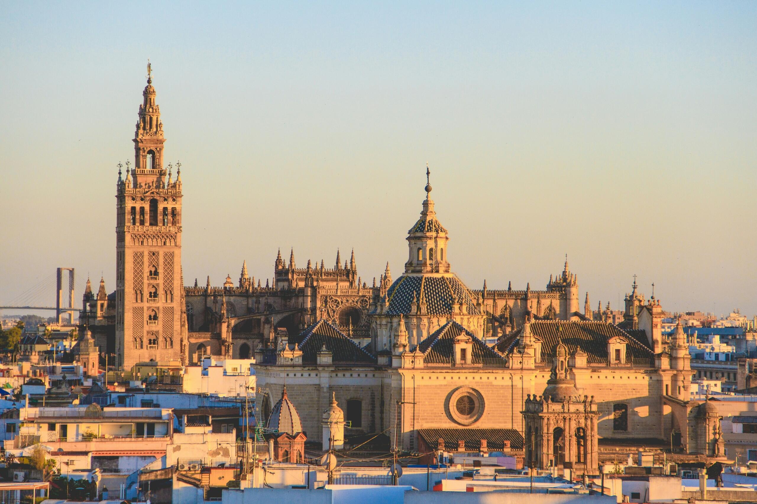 Panoramski pogled na Katedralo v Sevilli z ikoničnim zvonikom Giralda pri sončnem zahodu, obdano z mestnimi strehami