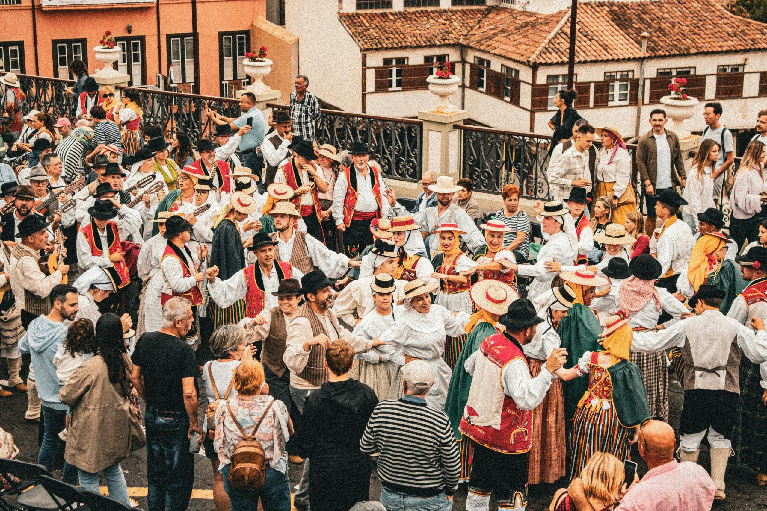 Skupina plesalcev v tradicionalnih kanarskih kostumih pleše na ulici med množico gledalcev na Tenerifeu