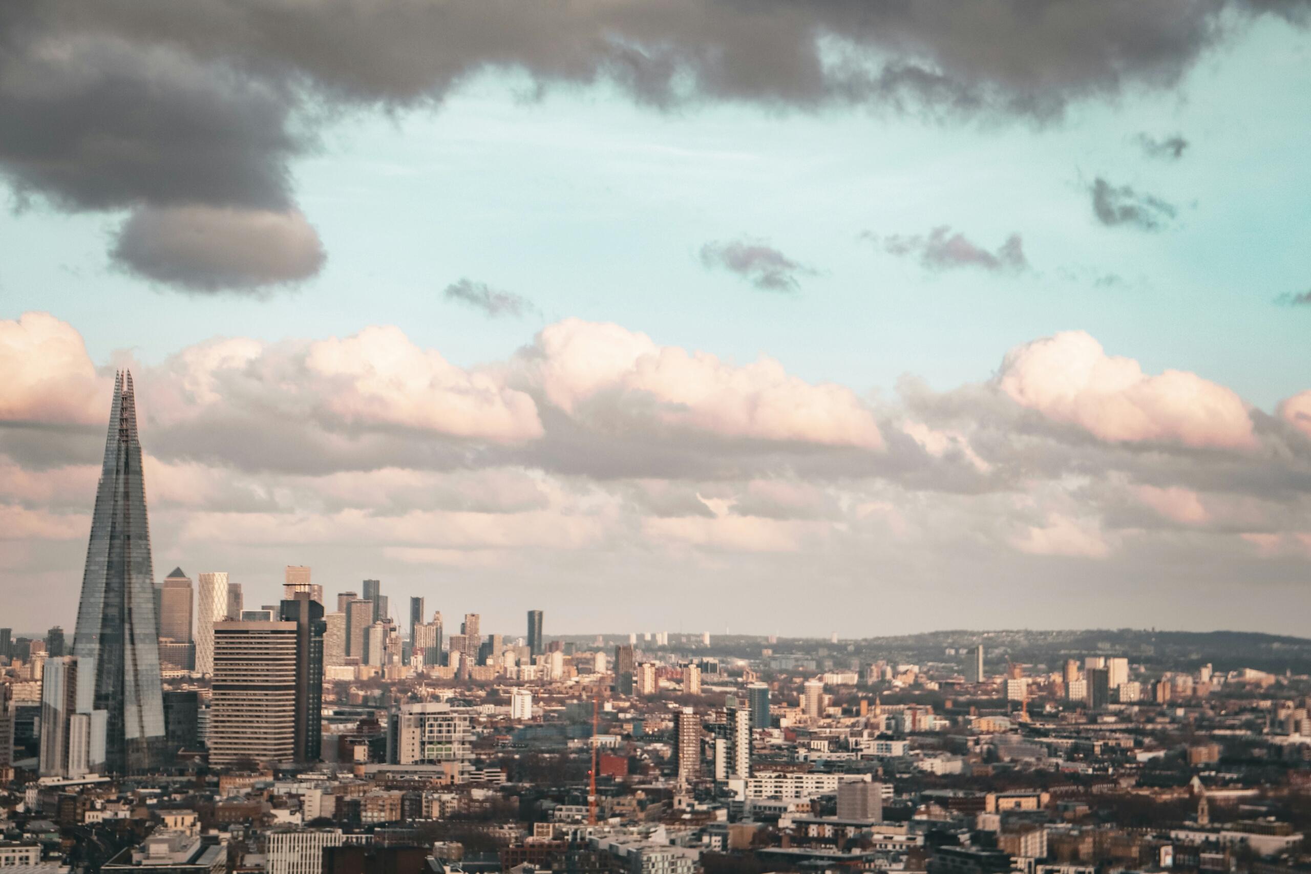 Panoramski pogled na londonsko obzorje z značilnim stolpom The Shard, oblaki v pastelnih odtenkih ob sončnem zahodu