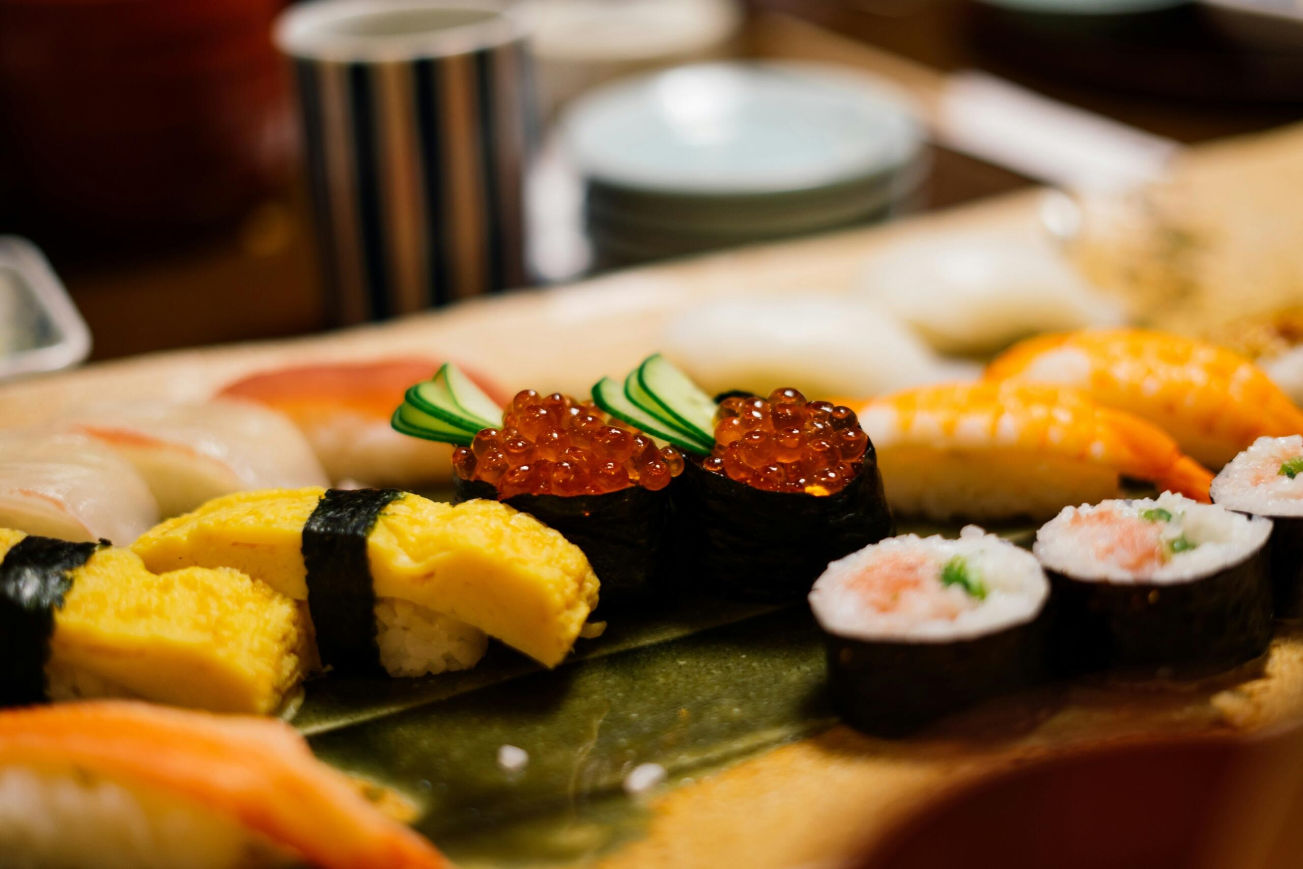 Svež sushi set na zelenem listu – tamago, ikura z avokadom, nigiri z lososom in kozicami ter maki zavitki