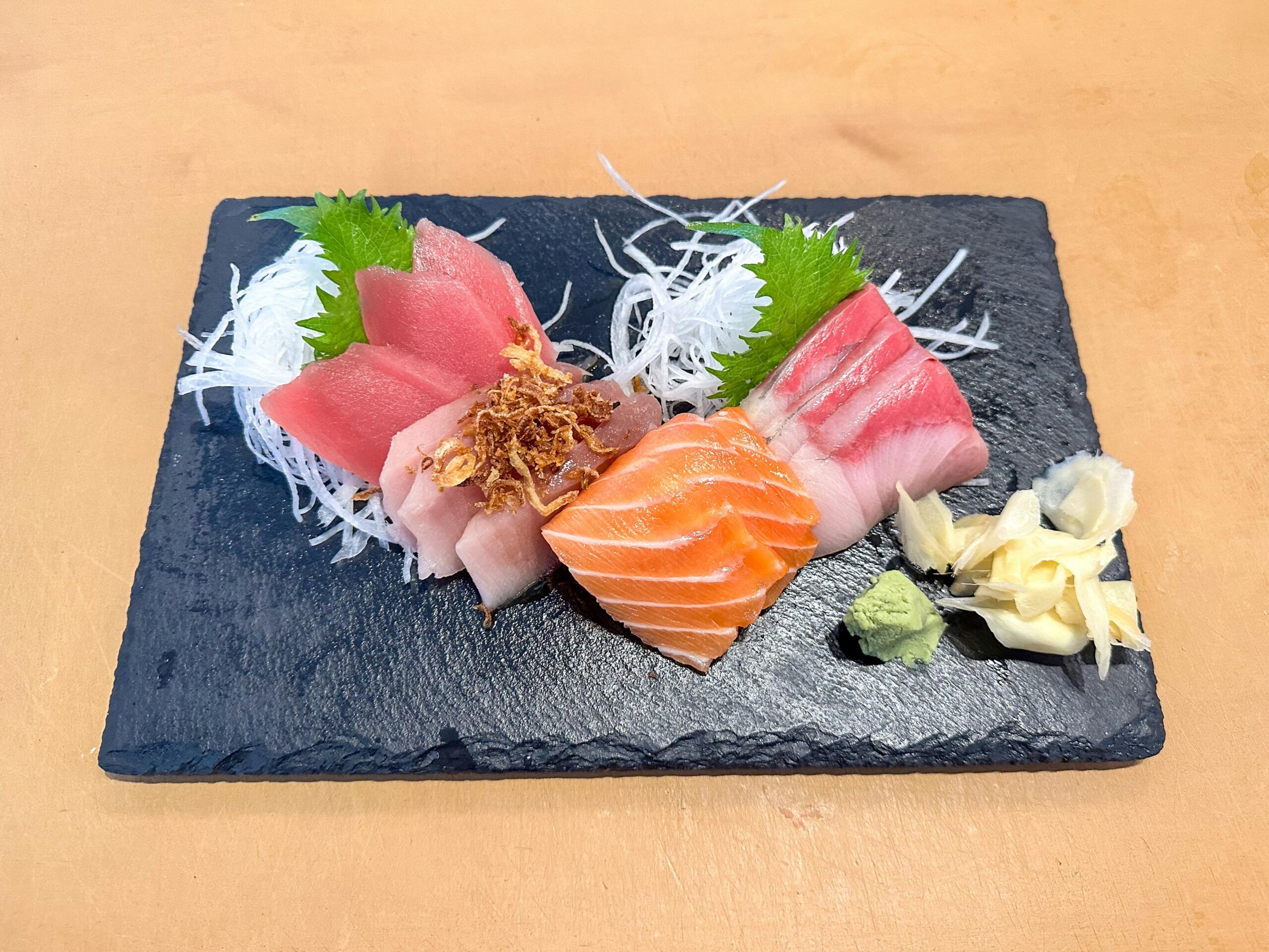 Svež sashimi na črnem kamnitem pladnju – rezinе tune, lososa in bele ribe z daikonom, shiso listi, wasabijem in ingverjem