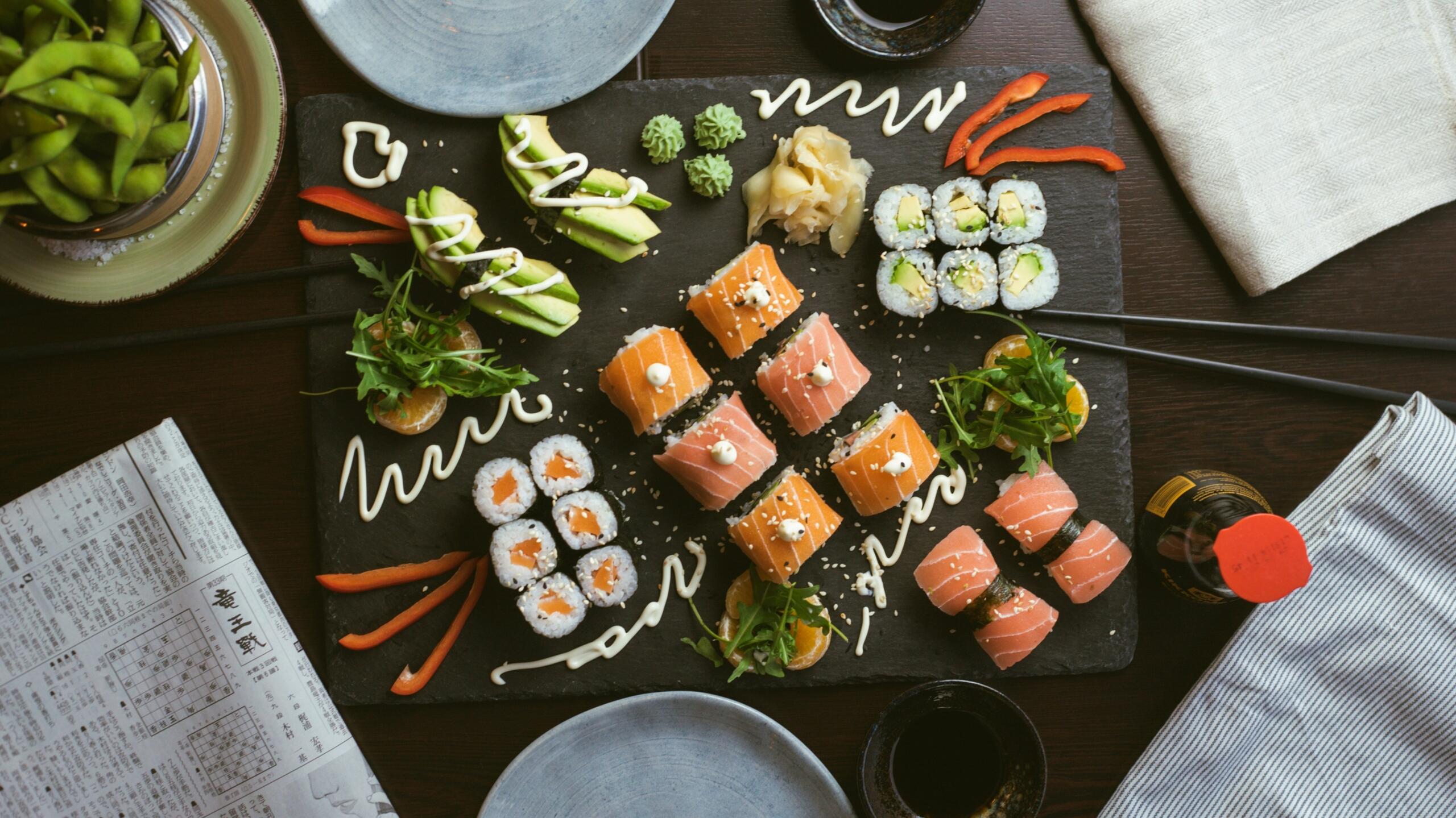 Pogled od zgoraj na velik sushi pladenj z lososovimi in avokadovimi rolami, wasabijem, ingverjem, avokadom, edamame in sojino omako