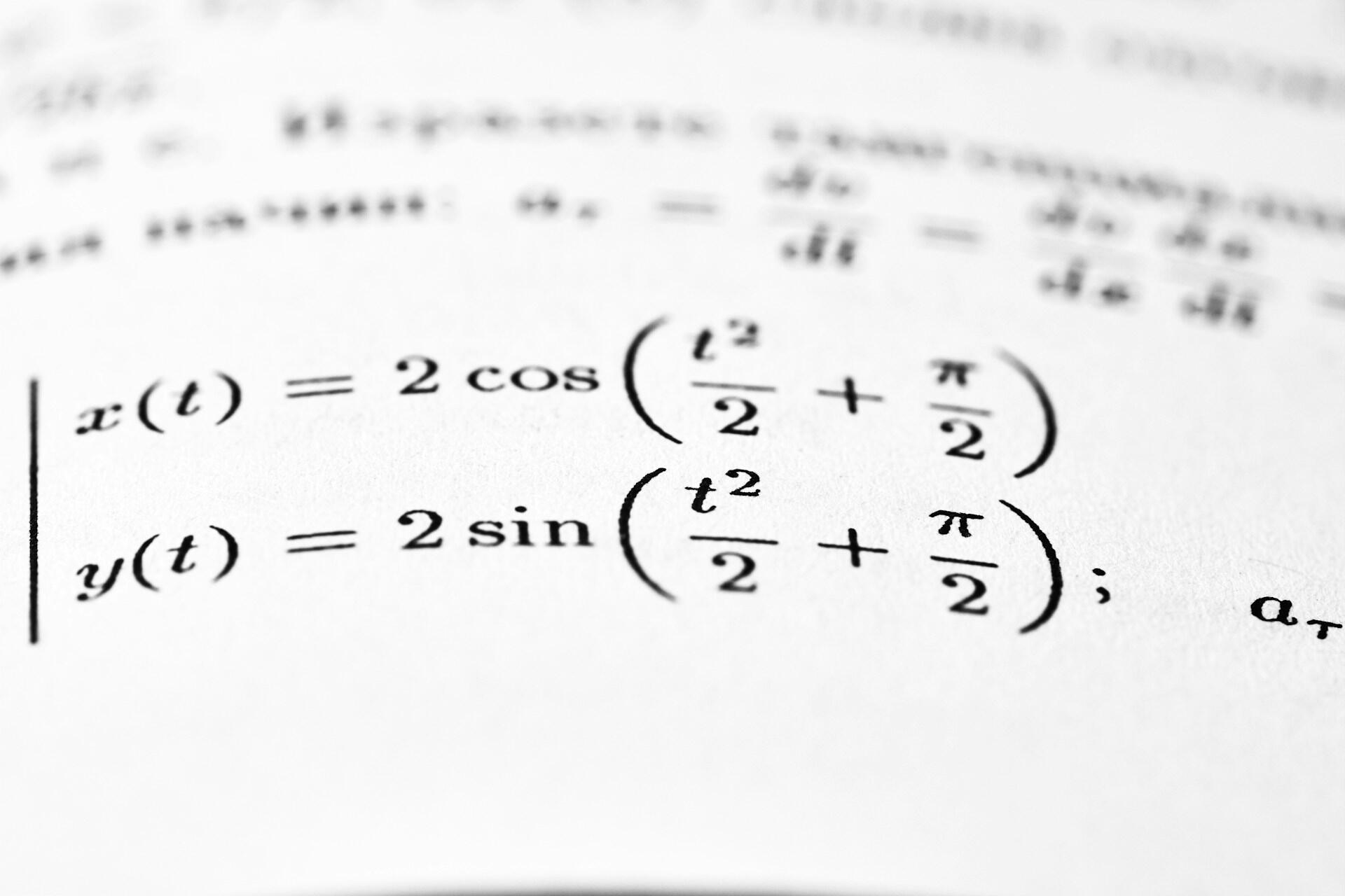 Matematické rovnice so sínusom a kosínusom vytlačené na papieri, rozmazané pozadie.
