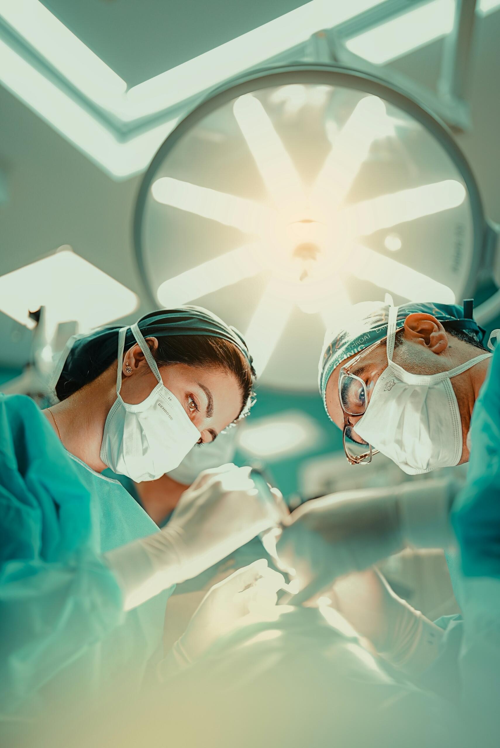 Chirurgička a chirurg so zakrytými tvárami pracujúci pod operačným svetlom