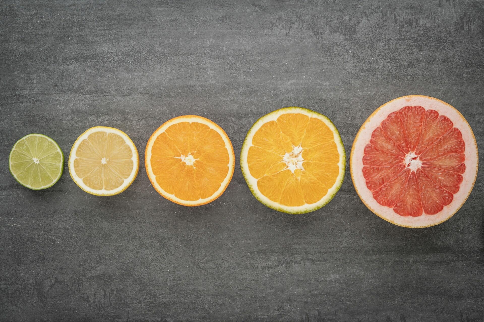 Prerezané citrusové plody zoradené podľa veľkosti na tmavom pozadí – od limetky po grep