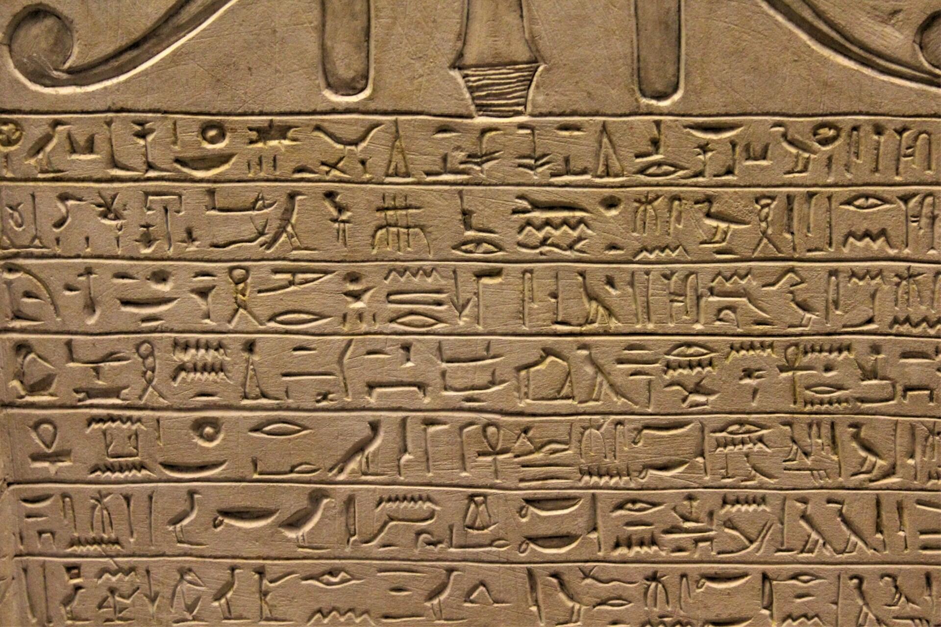 Detail staroegyptského nápisu s hieroglyfmi vyrytými do kameňa v horizontálnych líniách.