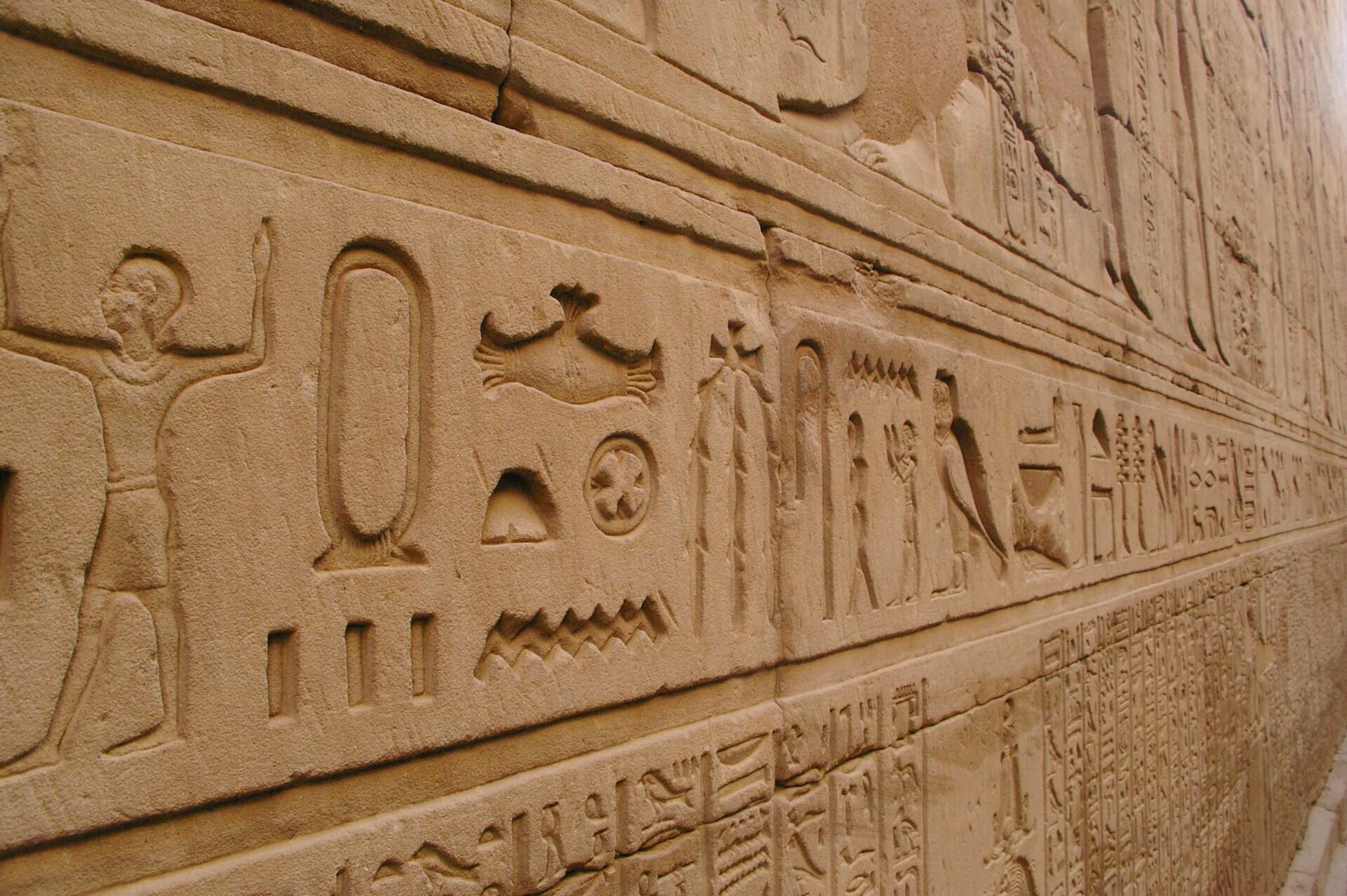 Stena staroegyptského chrámu pokrytá reliéfnymi hieroglyfmi a symbolmi.
