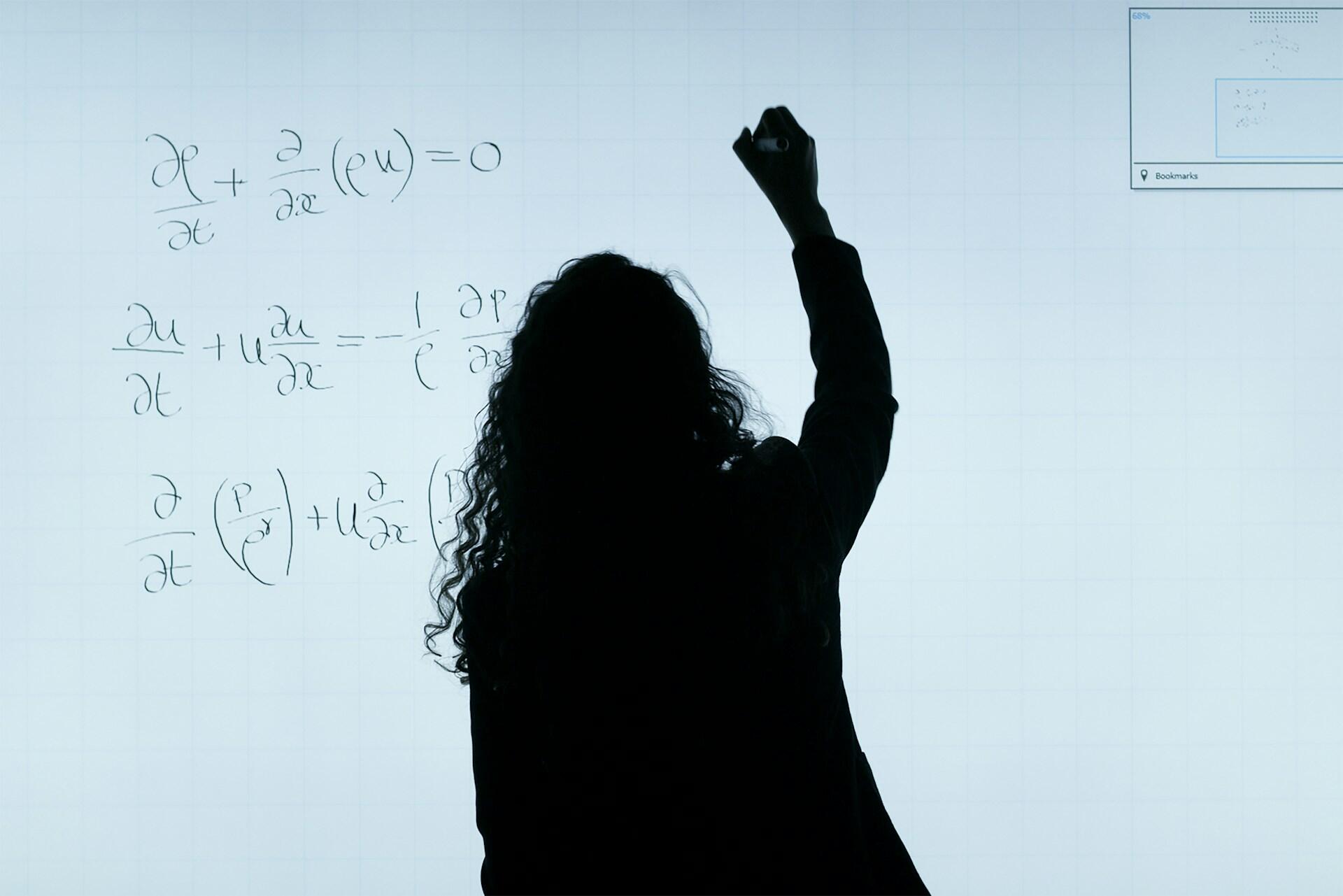 Osoba píšuca zložité matematické rovnice na svetelnú tabuľu alebo obrazovku.