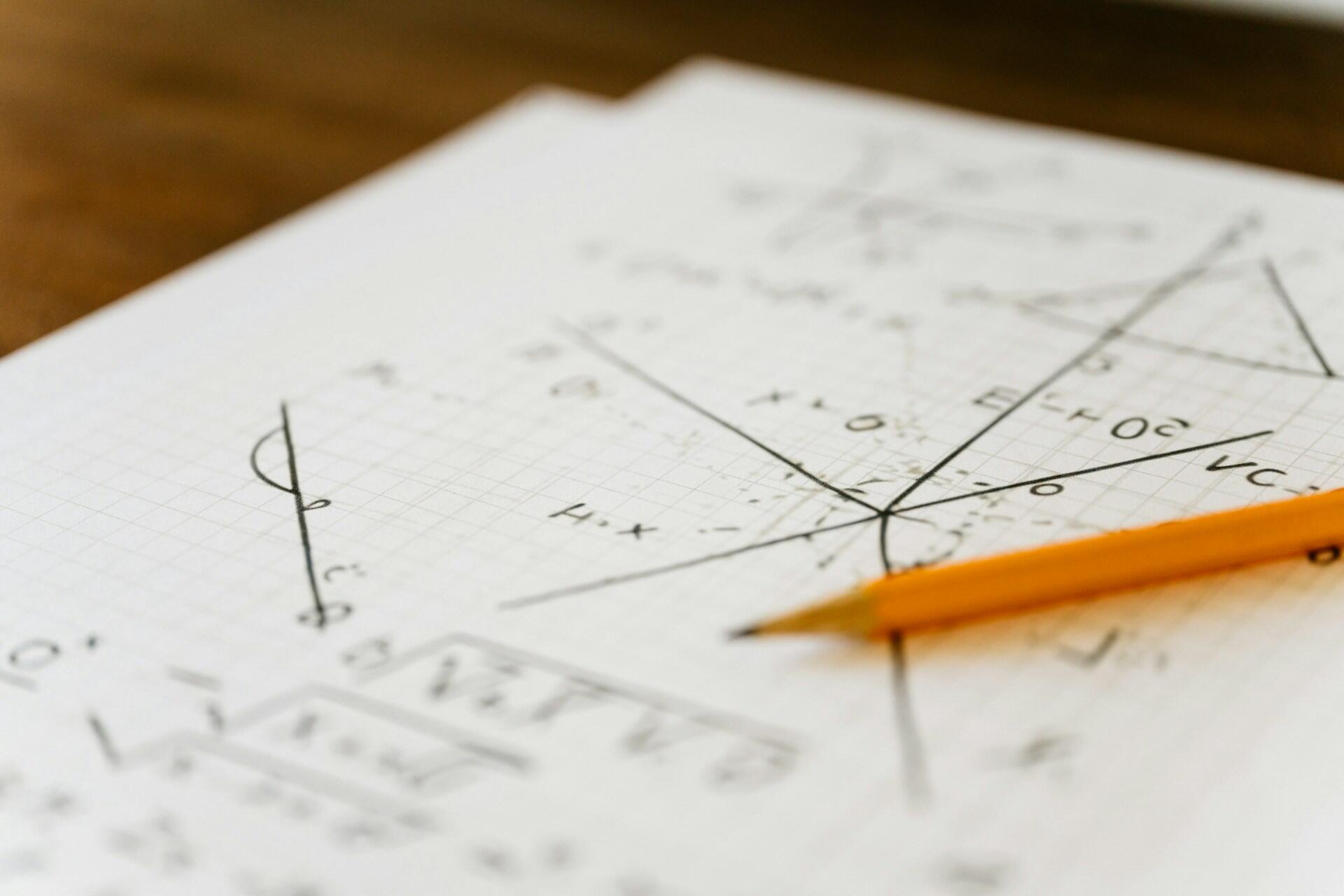 Matematické výpočty a grafy zakreslené na milimetrovom papieri s položenou ceruzkou.
