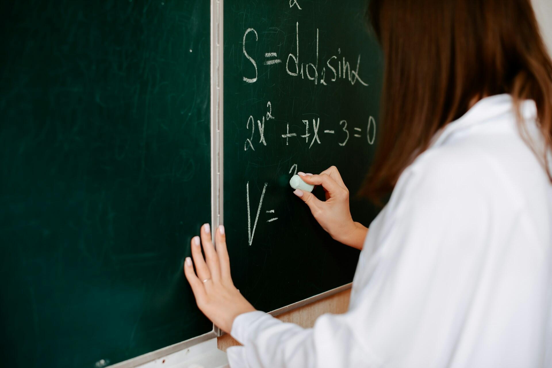 Žena píše matematické vzorce kriedou na zelenú školskú tabuľu.