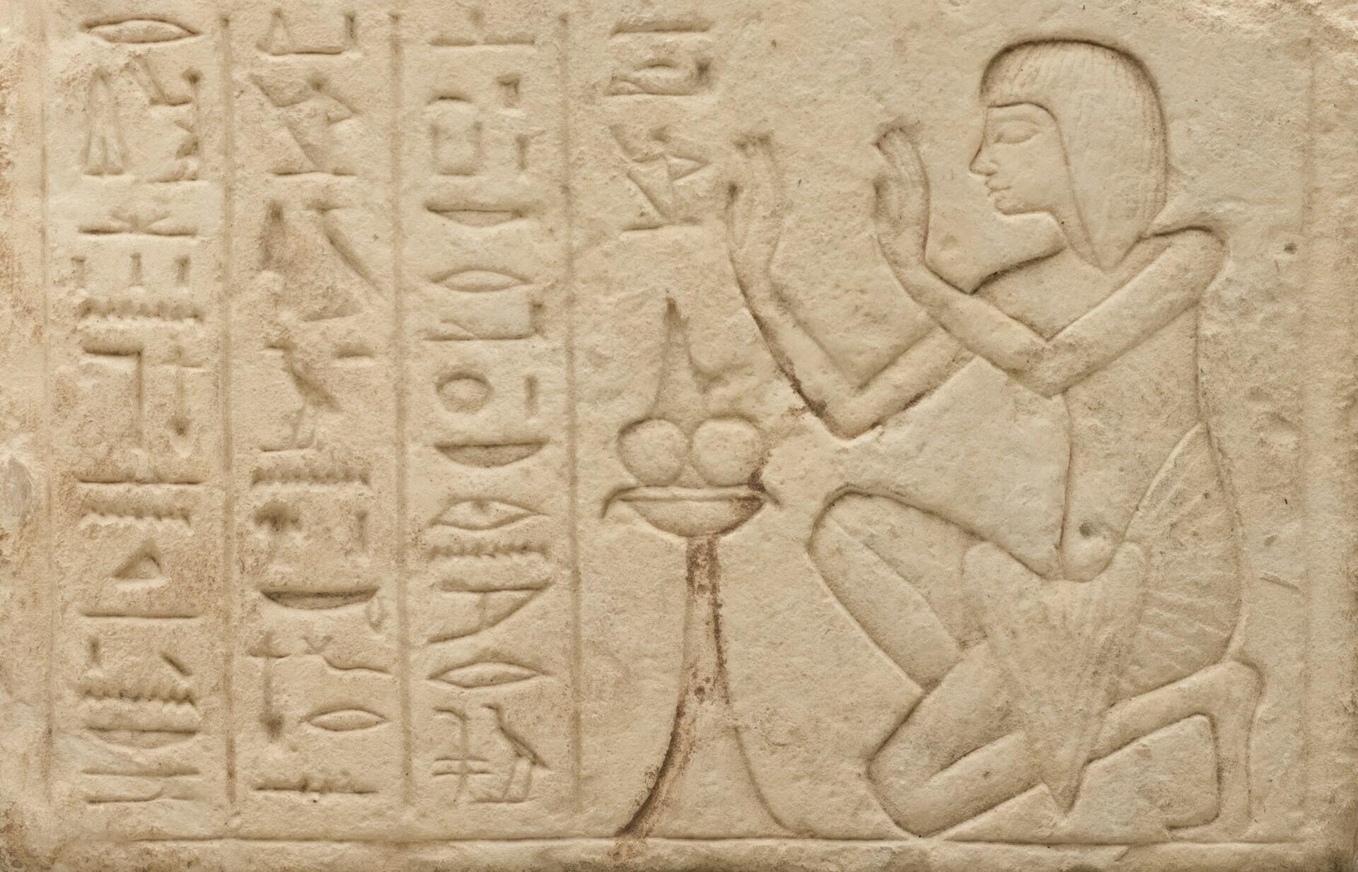 Staroveký egyptský reliéf s postavou a hieroglyfmi na pieskovcovom podklade.