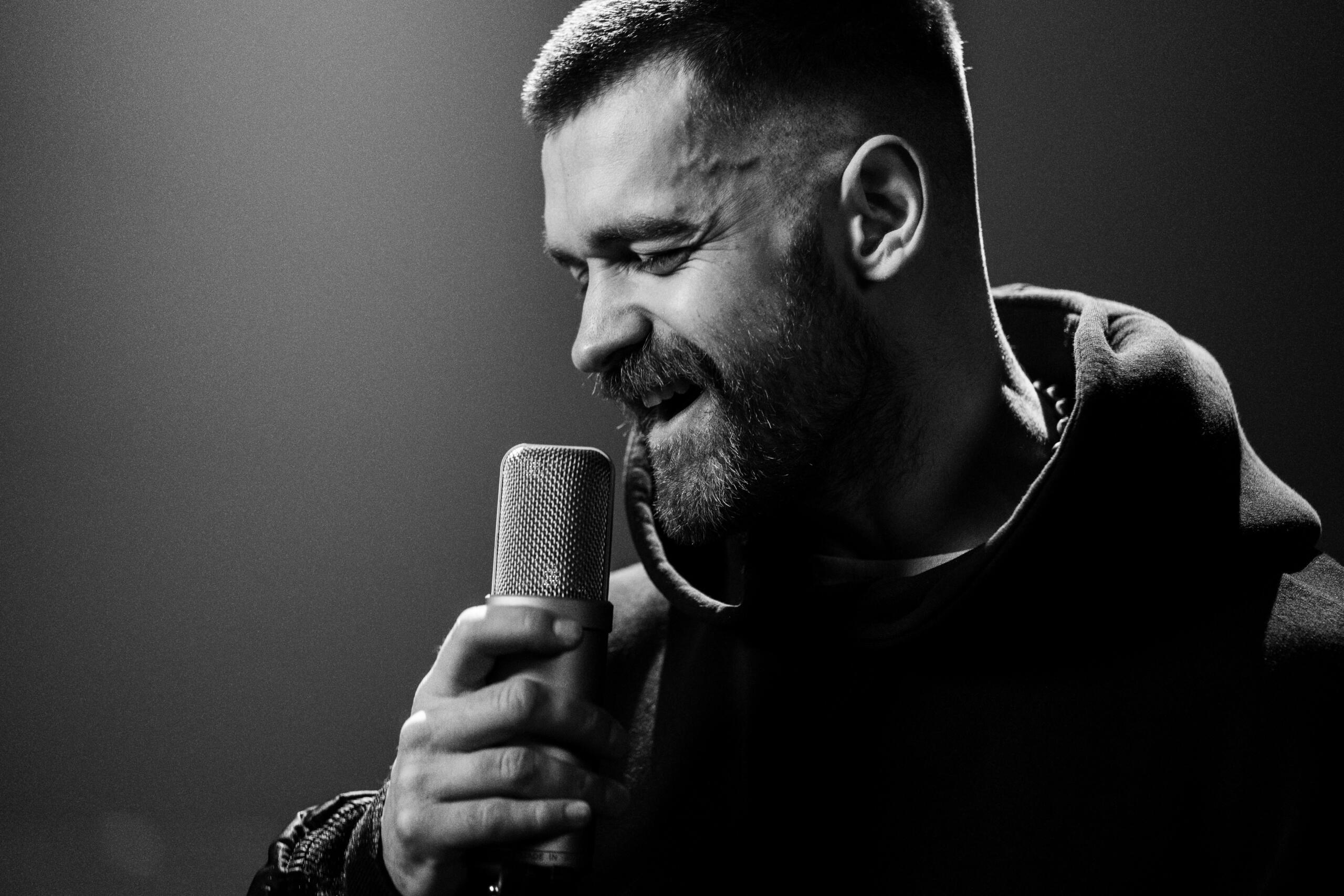Čiernobiela fotografia speváka spievajúceho do mikrofónu