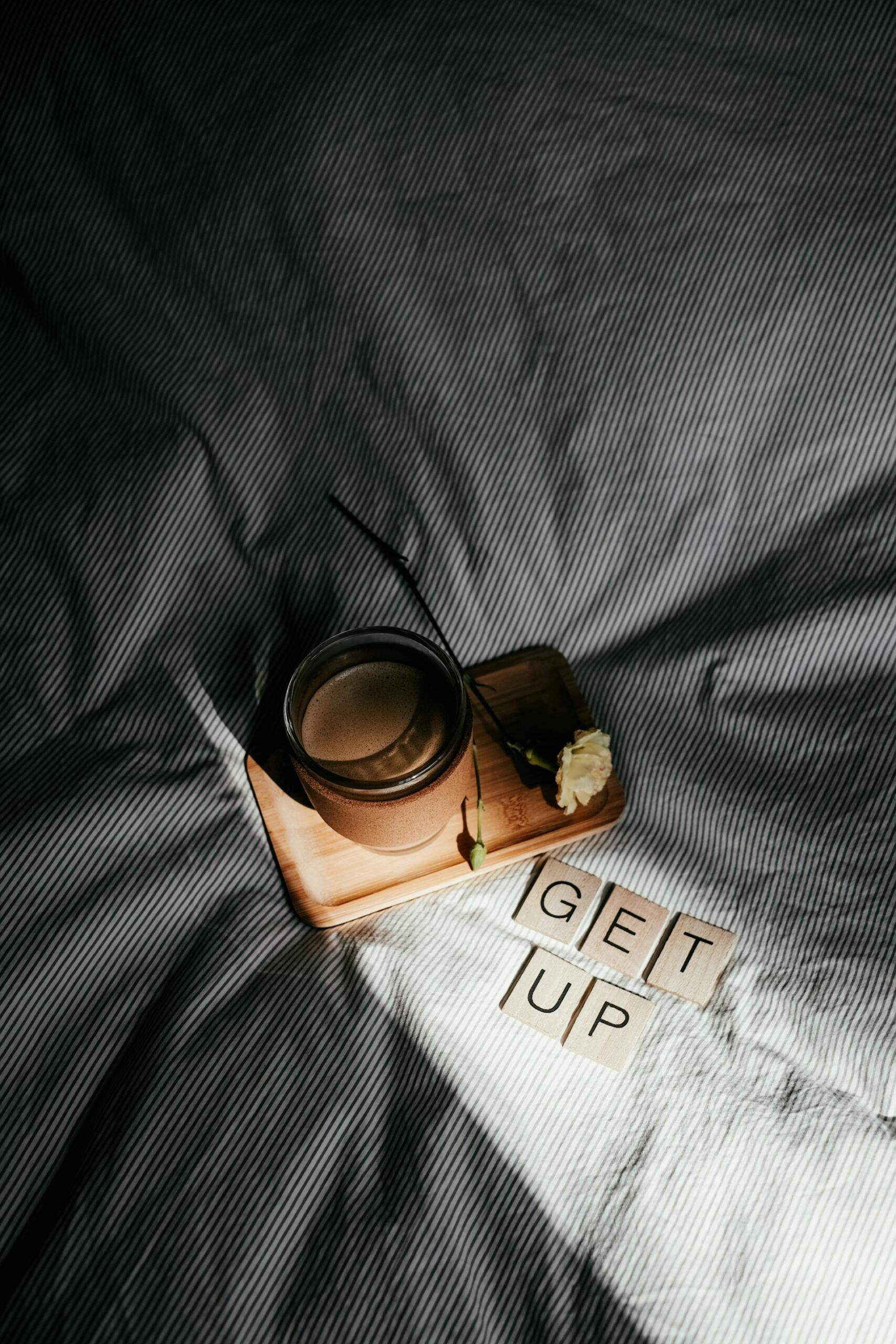 Motivačný nápis „Get up“ zložený z písmen na posteli vedľa šálky kávy
