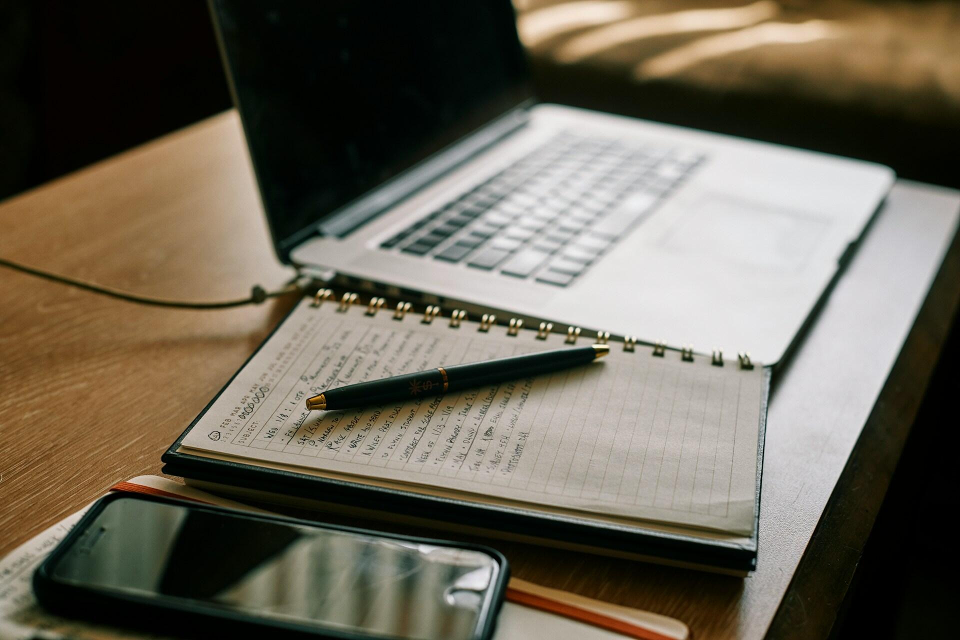 Zápisník s ručne písanými poznámkami položený vedľa notebooku.