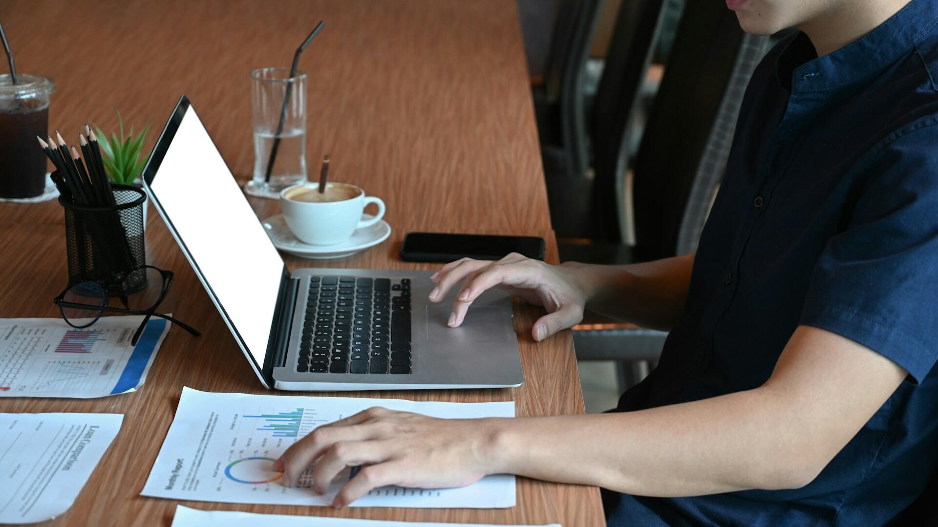 Študent pracuje na notebooku a prechádza si výsledky testu na tlačených dokumentoch.