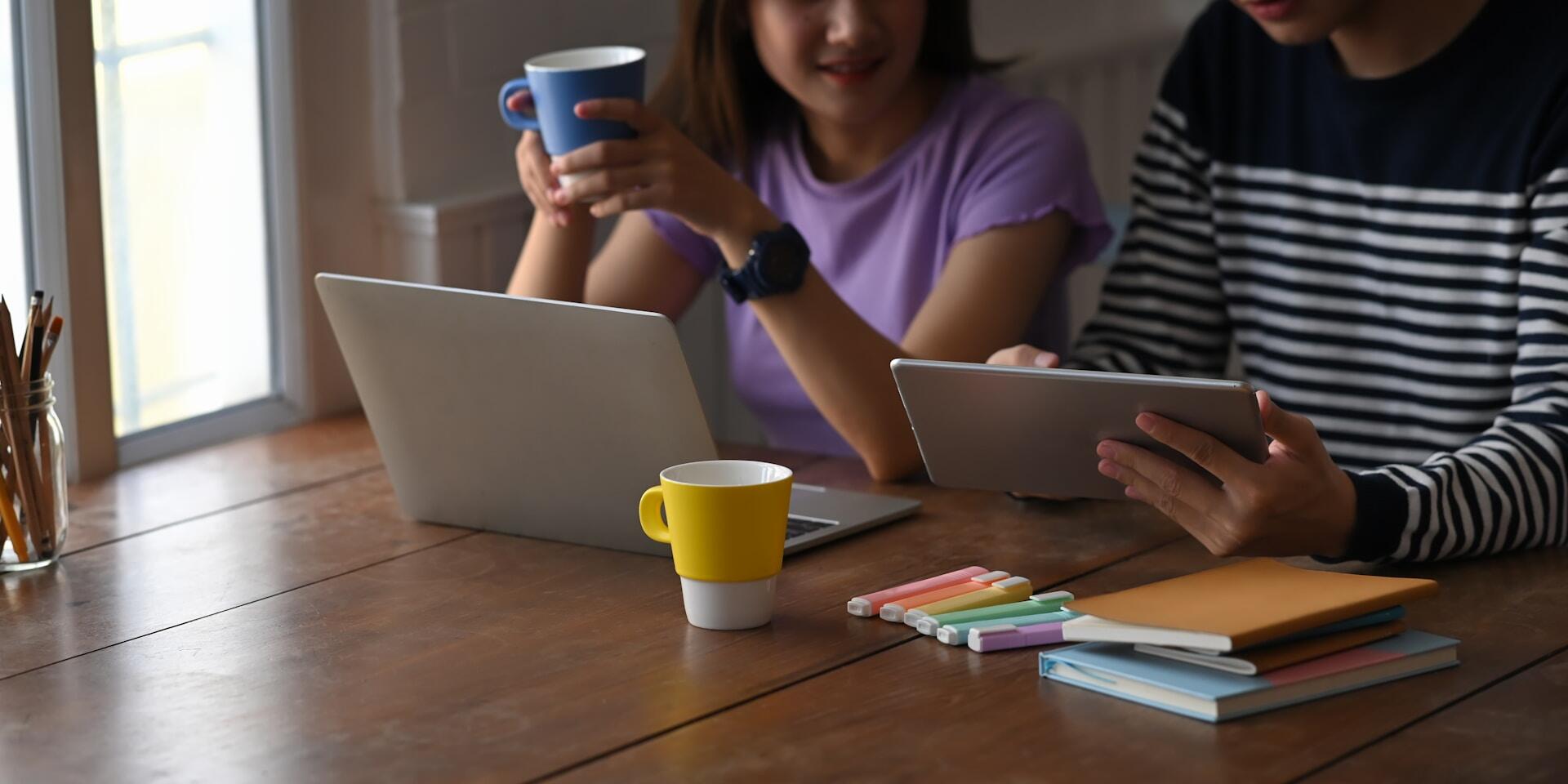 Dvaja mladí ľudia študujú s notebookom a tabletom pri káve.