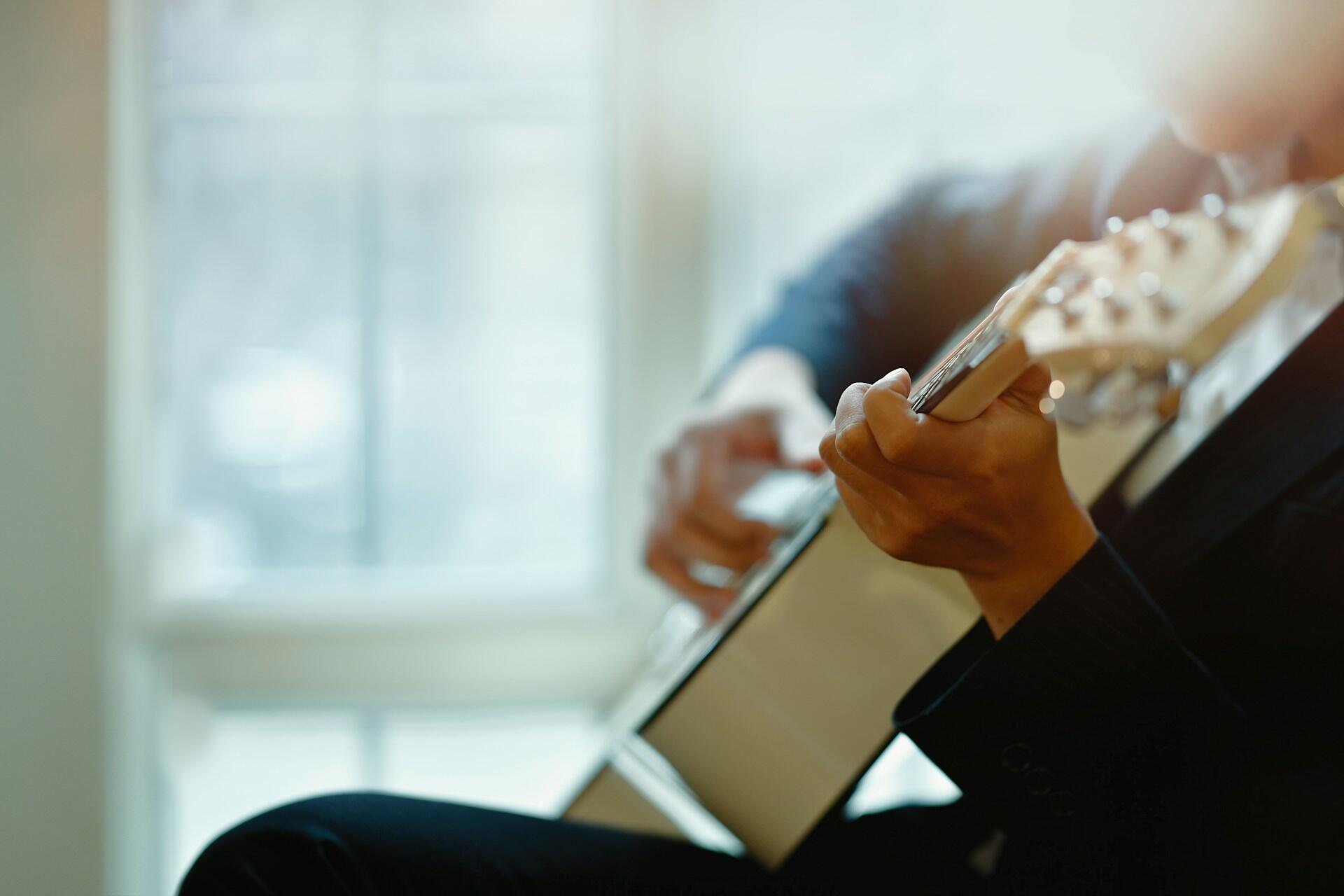 Muž hrajúci na akustickej gitare doma pri dennom svetle z okna