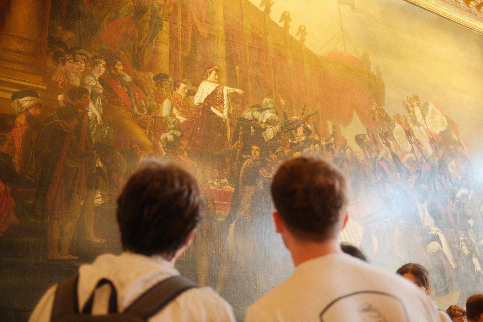 Návštevníci múzea sledujú historický obraz zobrazujúci revolučnú scénu s Napoleonom