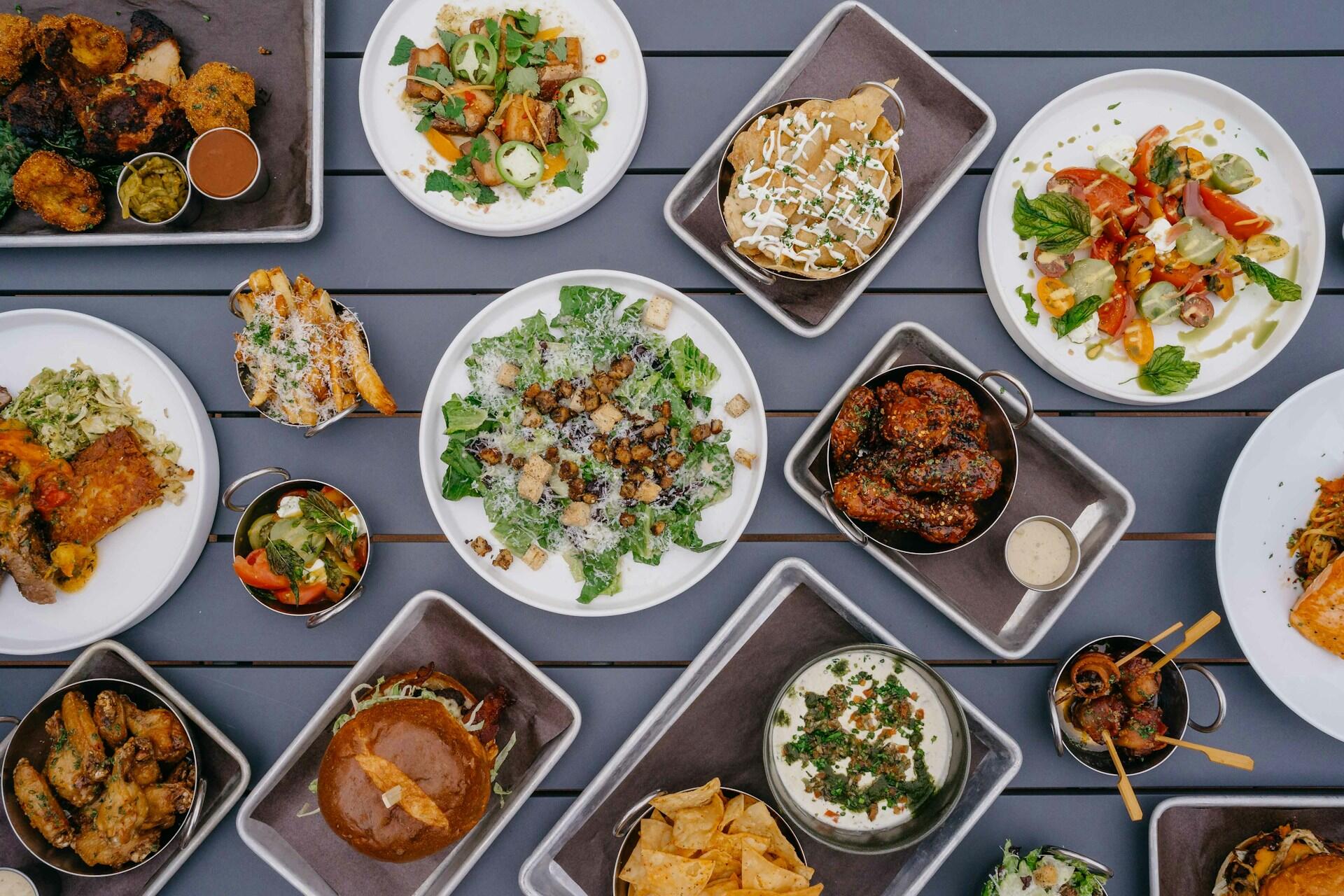 Bohato prestretý stôl plný rôznych jedál, šalátov, burgerov, omáčok a moderných gastro špecialít