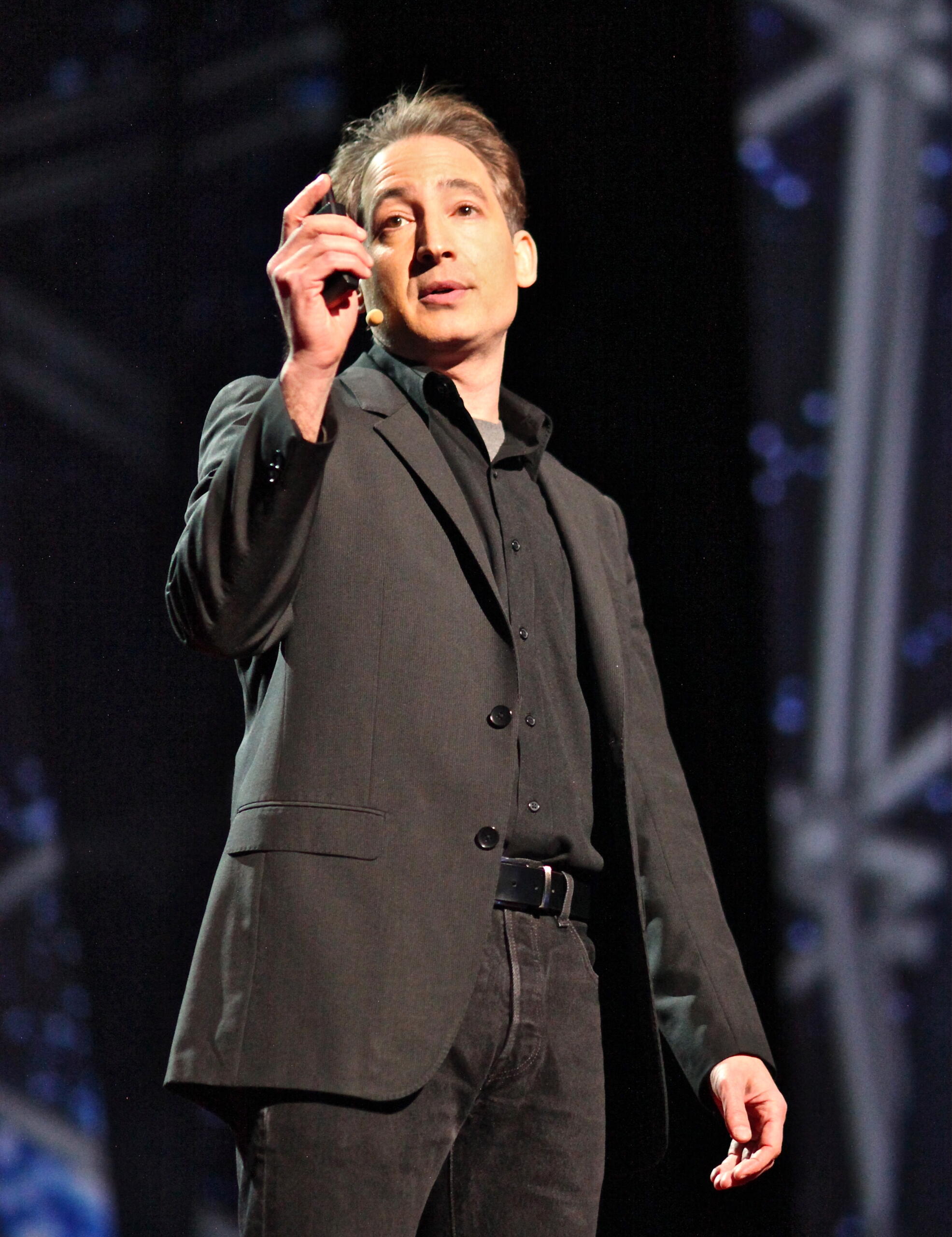 Brian Greene prednáša na vedeckej konferencii a drží v ruke diaľkový ovládač prezentácie
