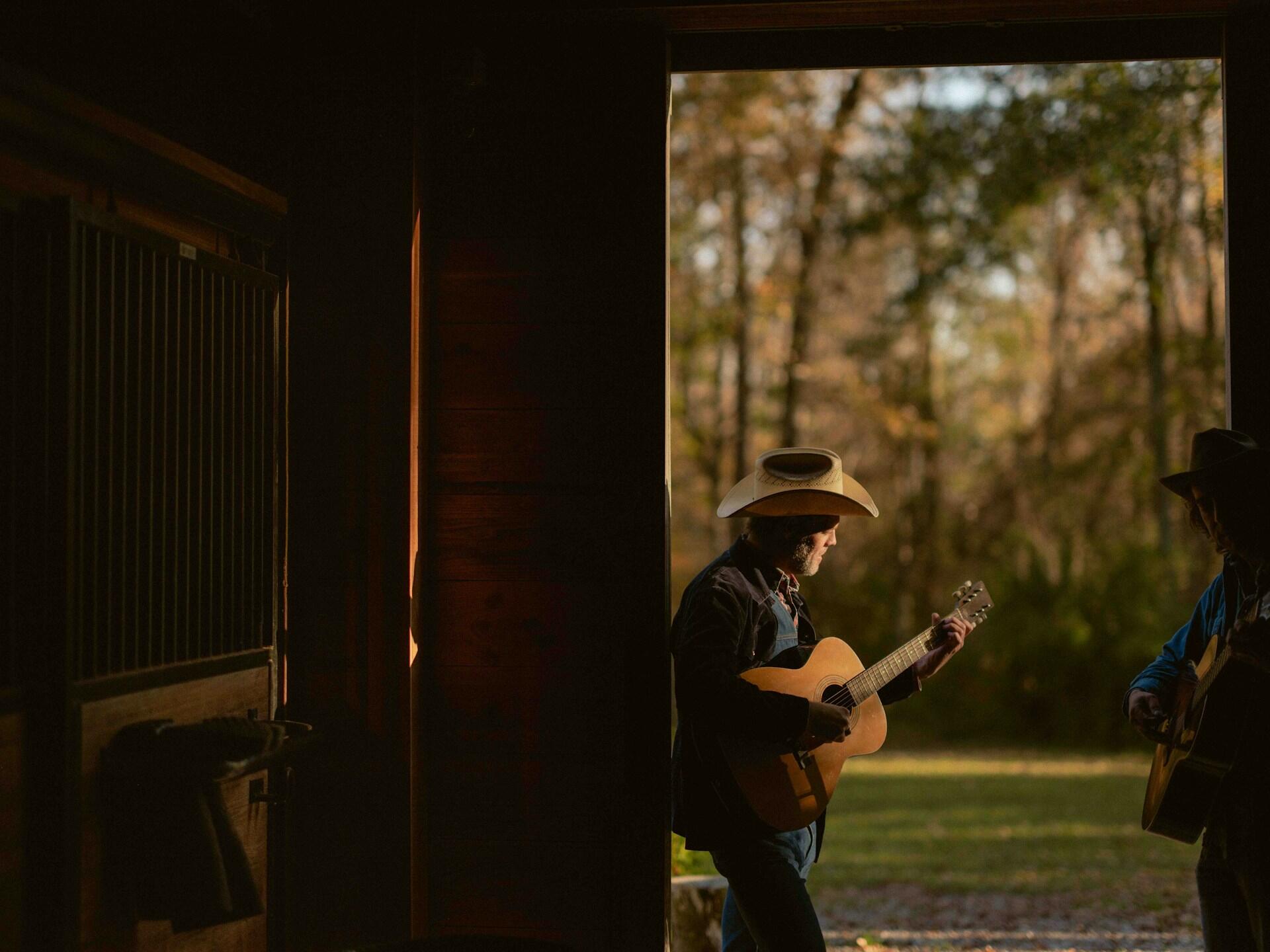 Dvaja country hudobníci hrajú na akustických gitarách pri otvorených dverách stodoly