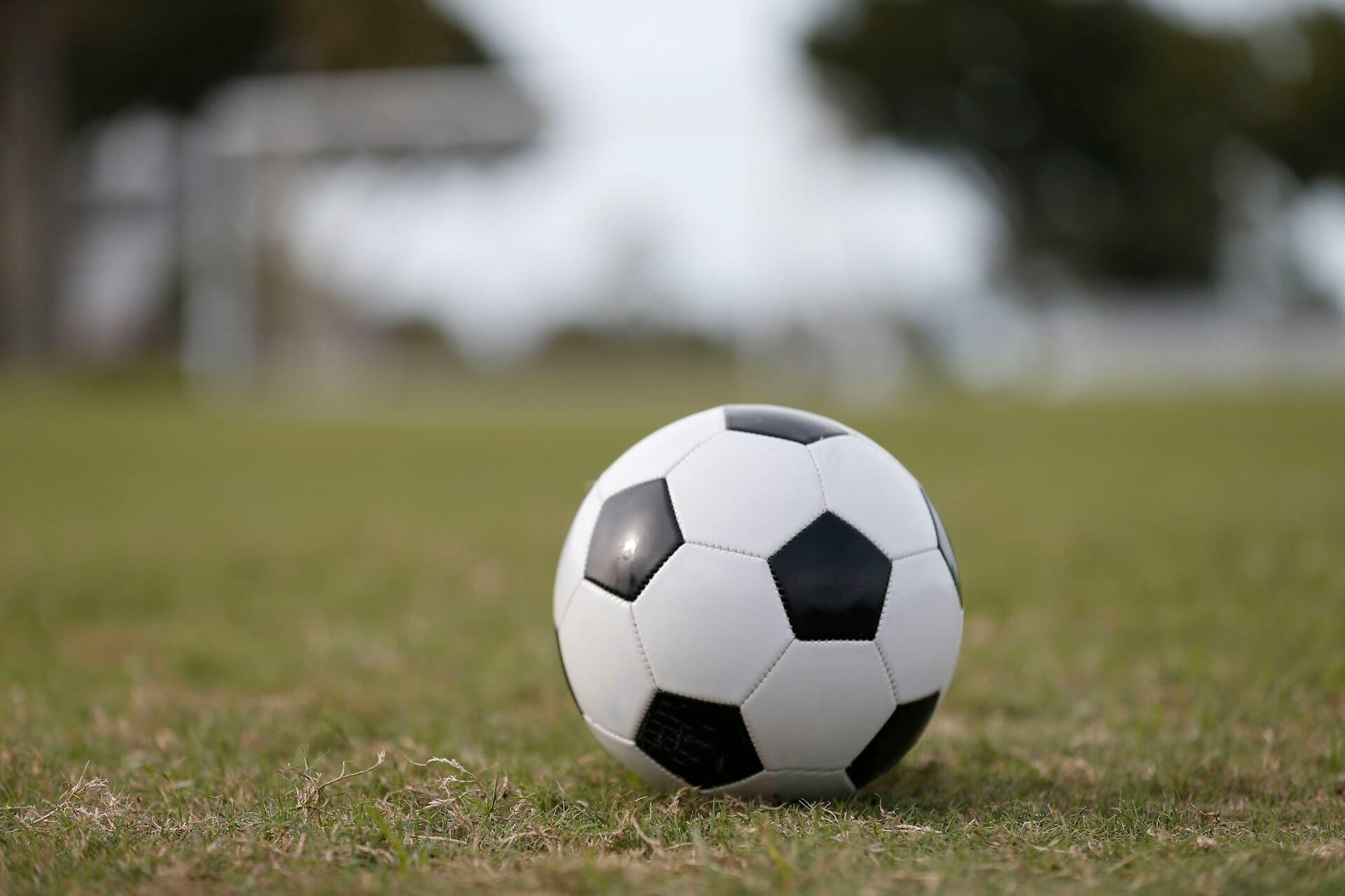 Futbalová lopta položená na trávniku s rozmazanou bránou v pozadí