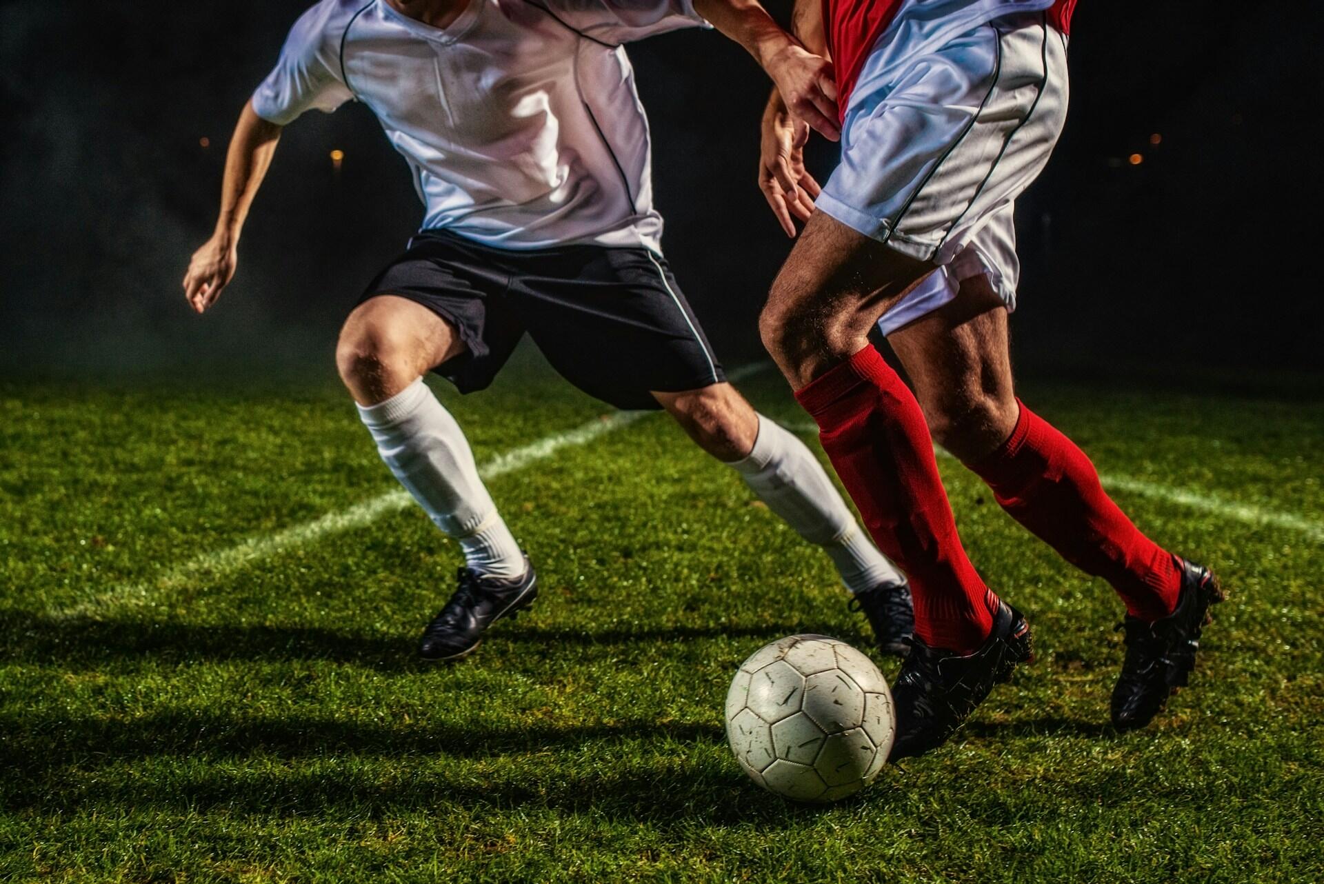 Dvaja futbalisti bojujú o loptu počas nočného zápasu na trávniku