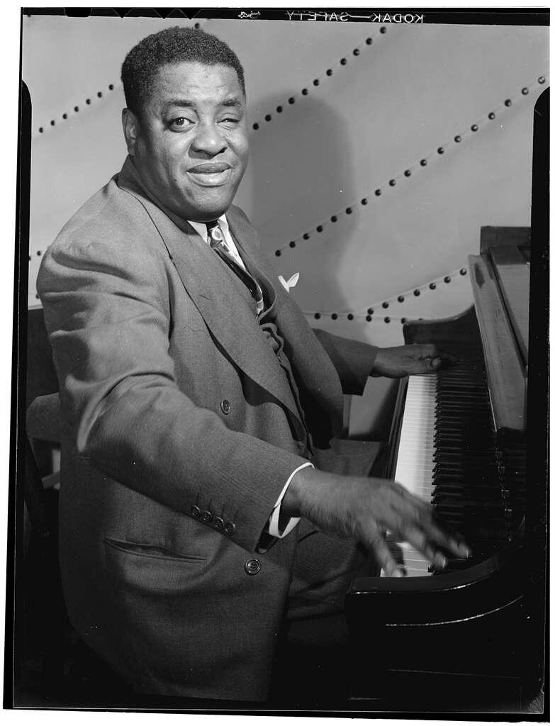 Legendárny jazzový klavirista Art Tatum hrá na klavíri počas vystúpenia. Čiernobiela fotografia zachytáva jeho charakteristický úsmev a virtuóznu hru na klávesoch.