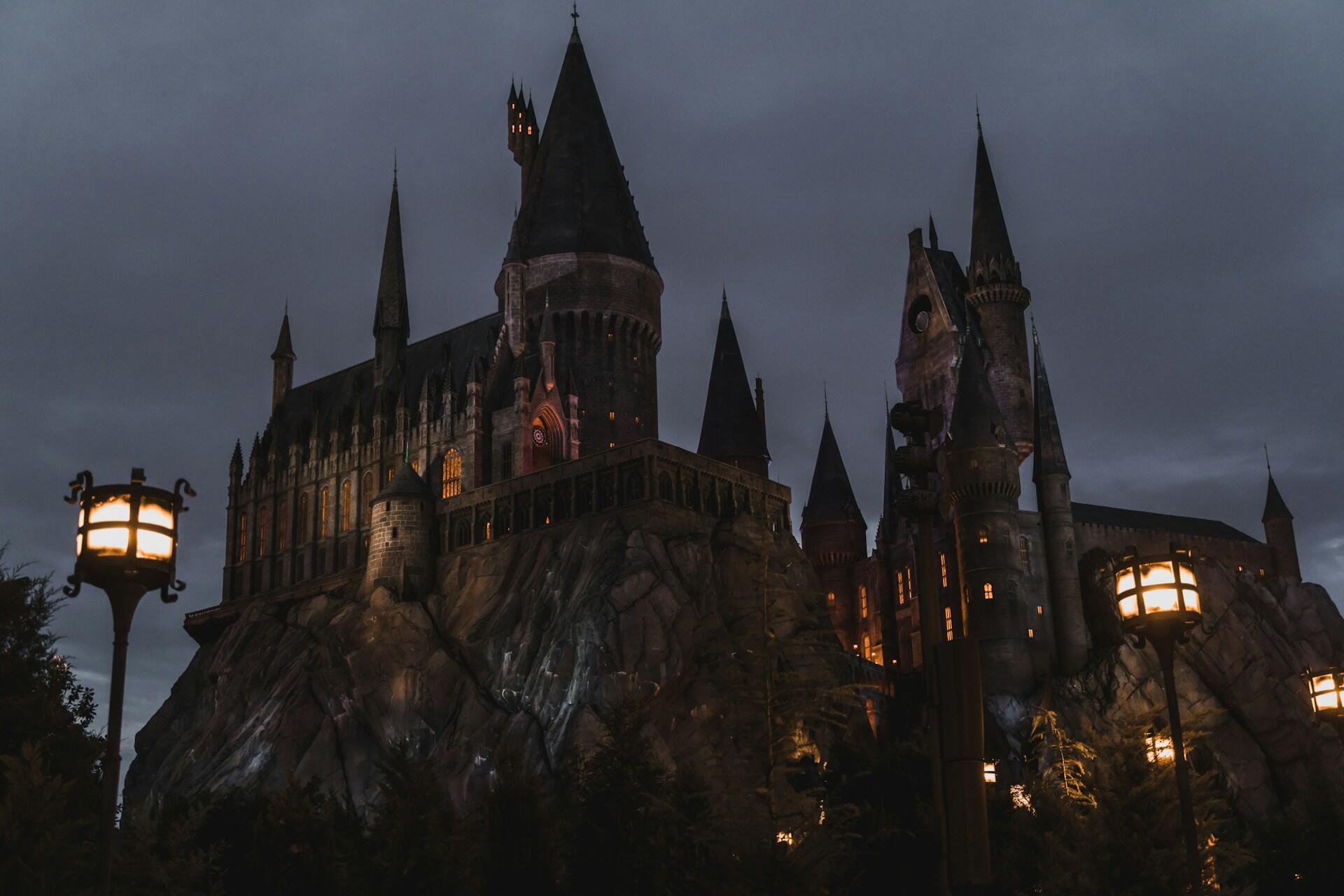Nočný pohľad na Rokfortský hrad z Harryho Pottera, osvetlený lampami a týčiaci sa na skalnatom útese.