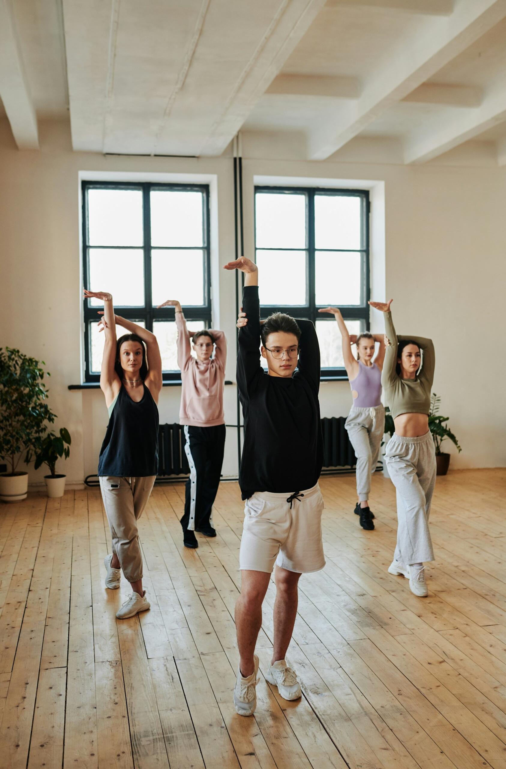 Skupina mladých ľudí cvičí tanečnú choreografiu v svetlom tanečnom štúdiu.