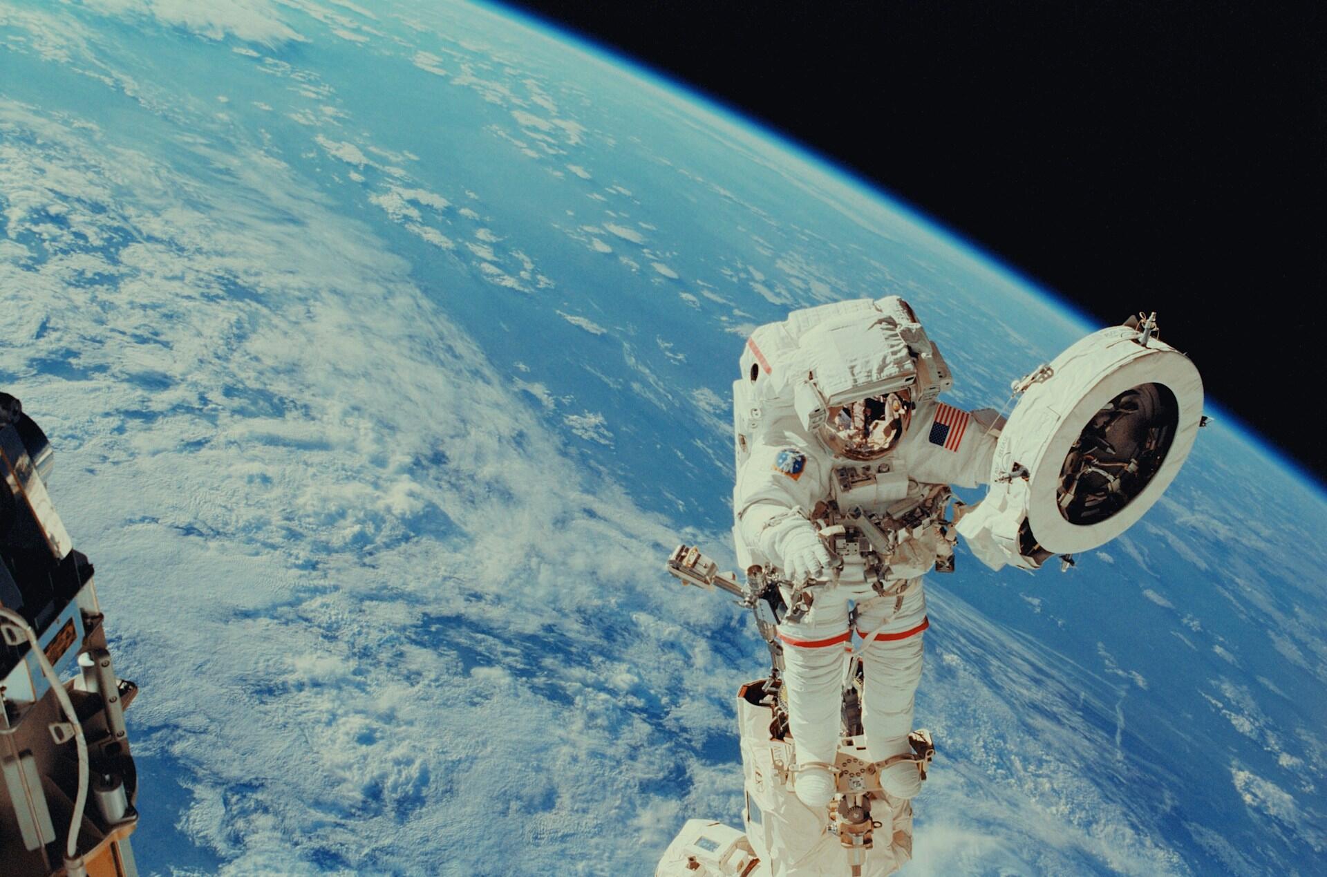 Astronaut počas výstupu do otvoreného vesmíru s planétou Zem v pozadí.