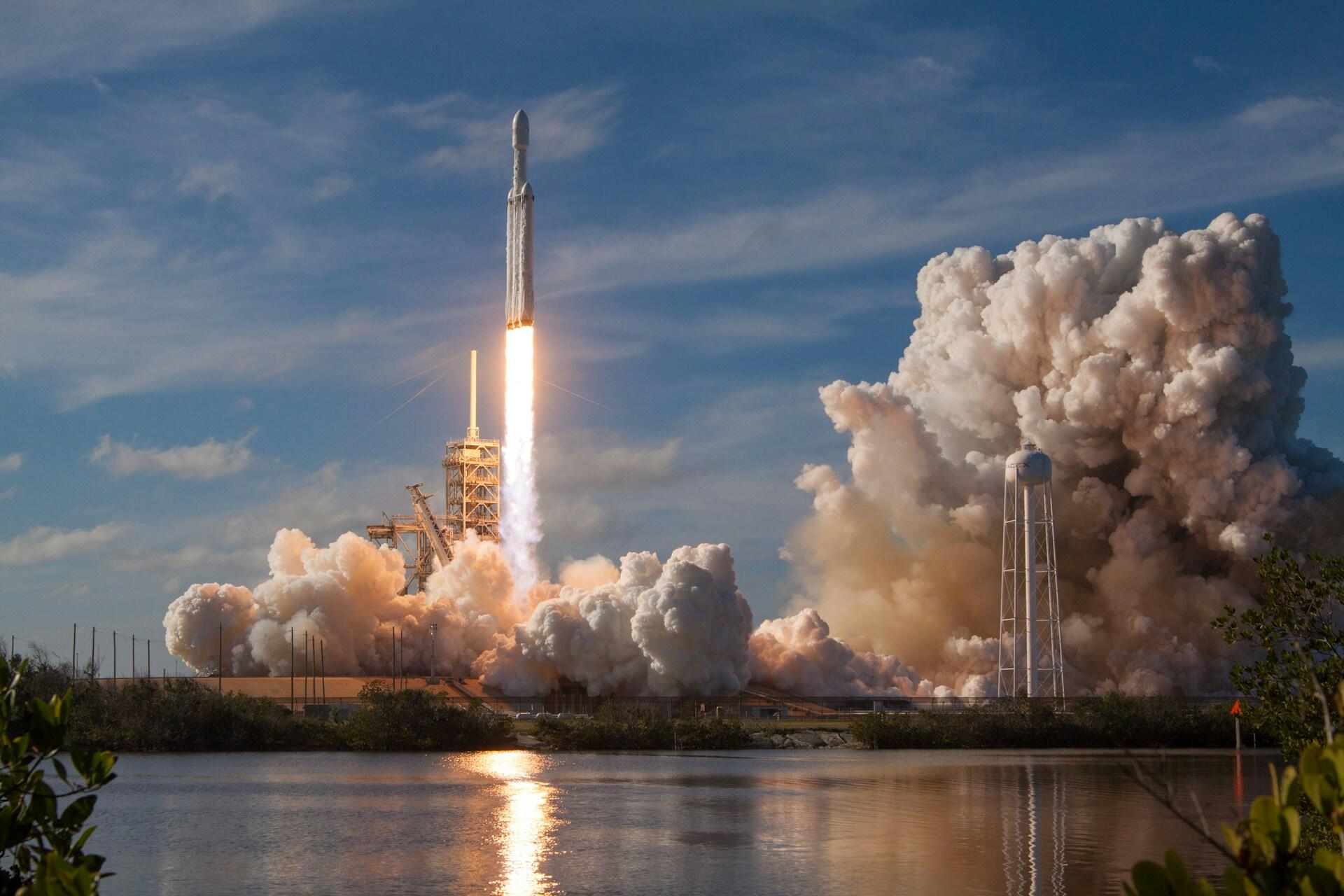 Štart rakety z kozmodrómu sprevádzaný mohutným oblakom dymu a plameňmi z raketových motorov.