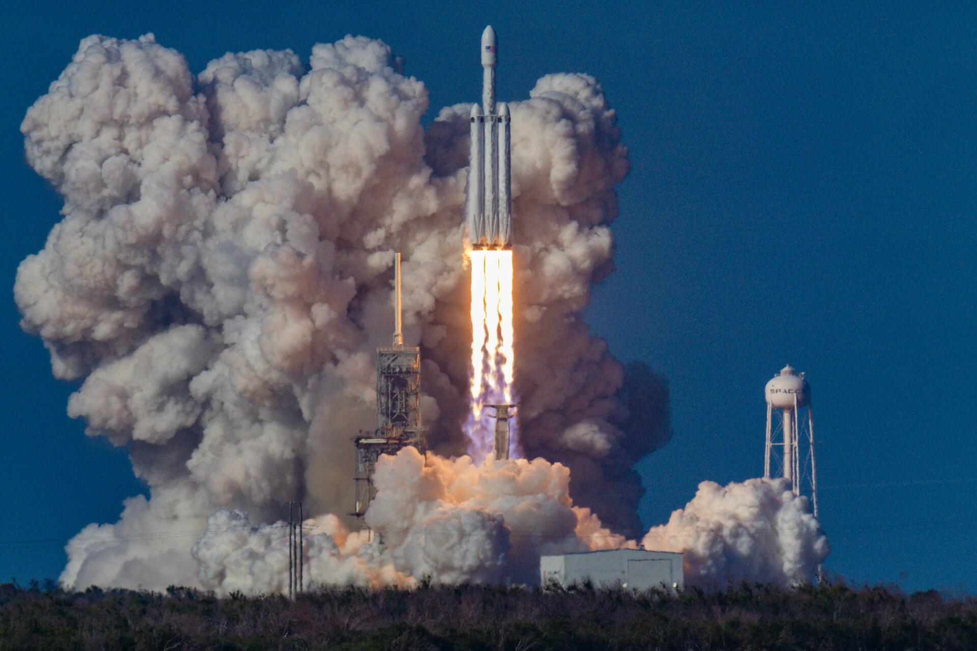 Štart rakety do vesmíru z odpaľovacej rampy sprevádzaný mohutnými oblakmi dymu.