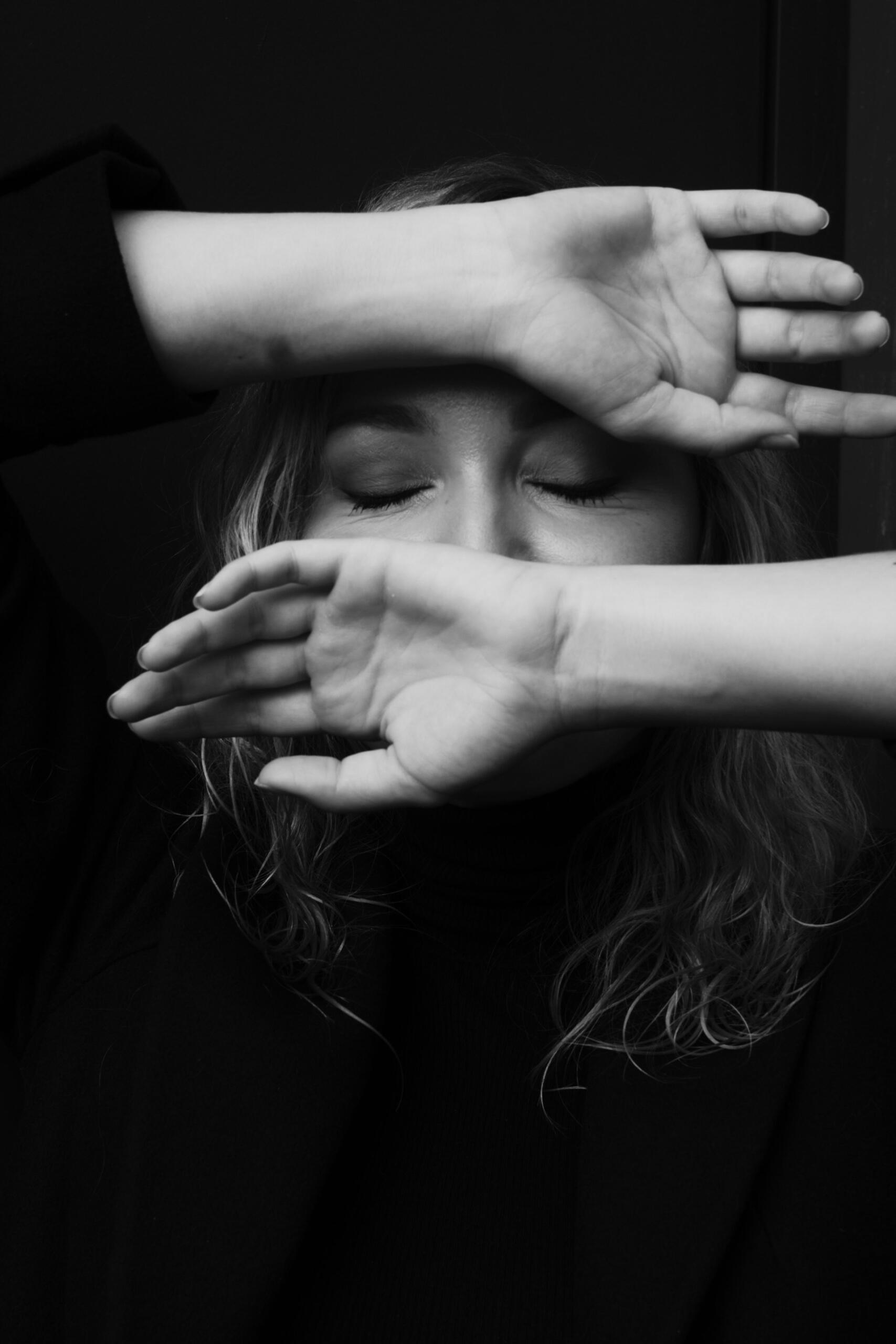 Čiernobiela fotografia ženy so zatvorenými očami a rukami pred tvárou, ktorá pôsobí unavene a emocionálne vyčerpane.