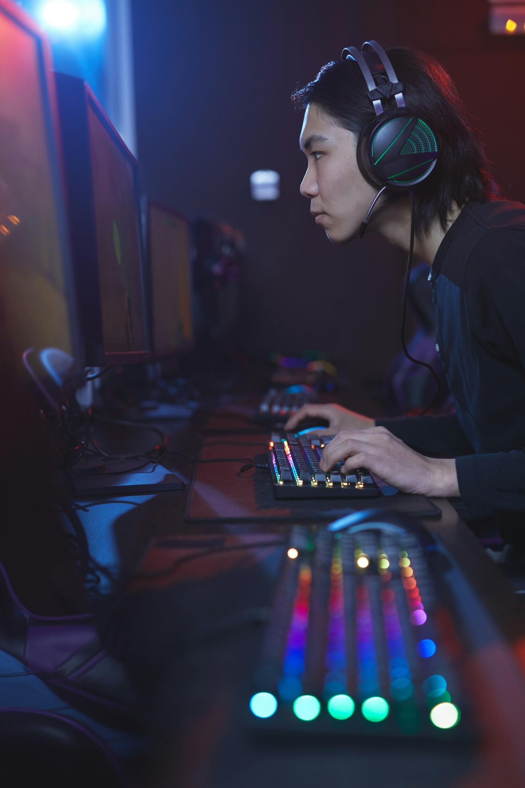 Hráč so slúchadlami hrá počítačovú hru na hernom PC s podsvietenou klávesnicou.