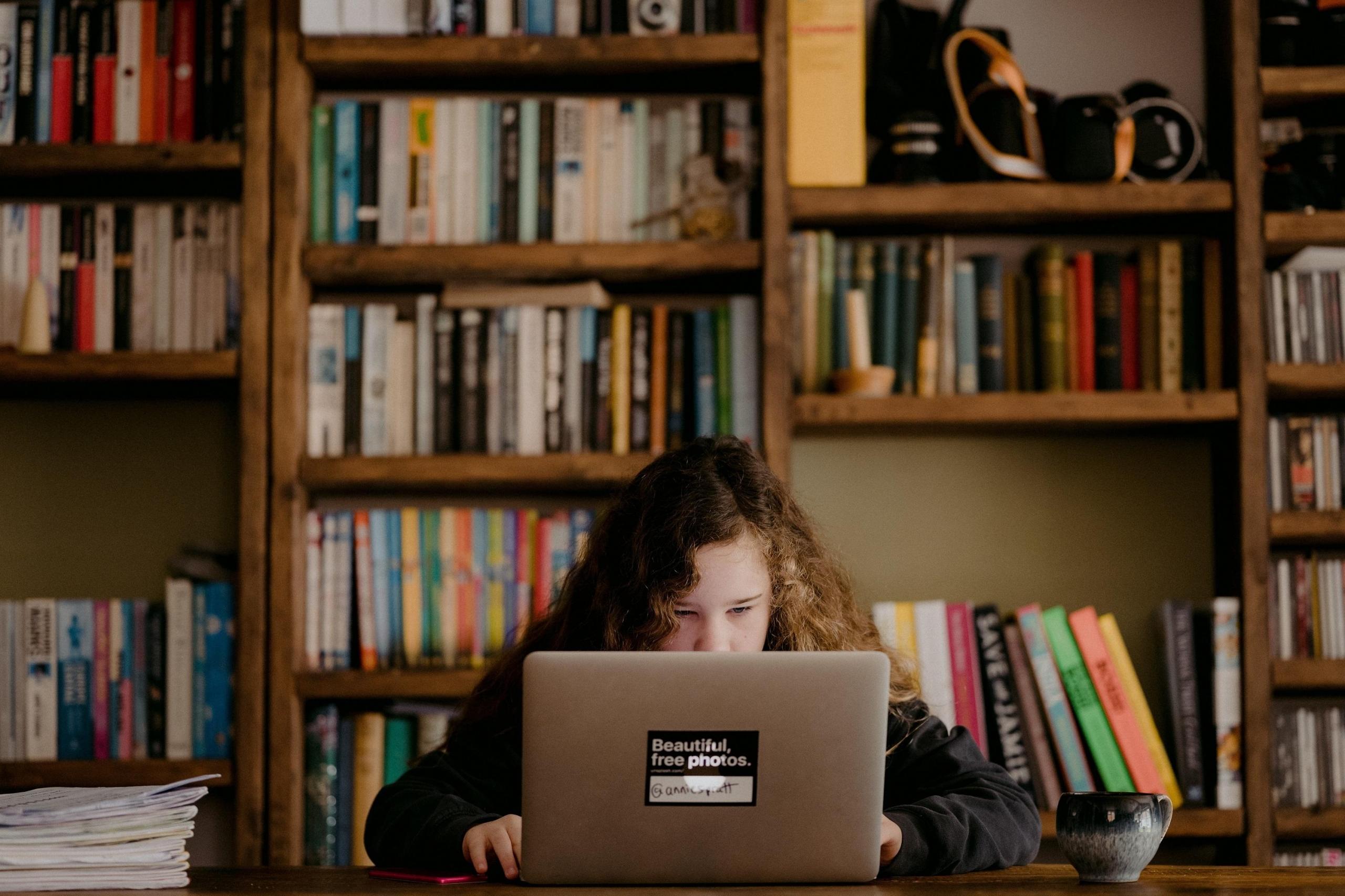 Kitaplığın önünde laptoptan ders çalışan kız öğrenci